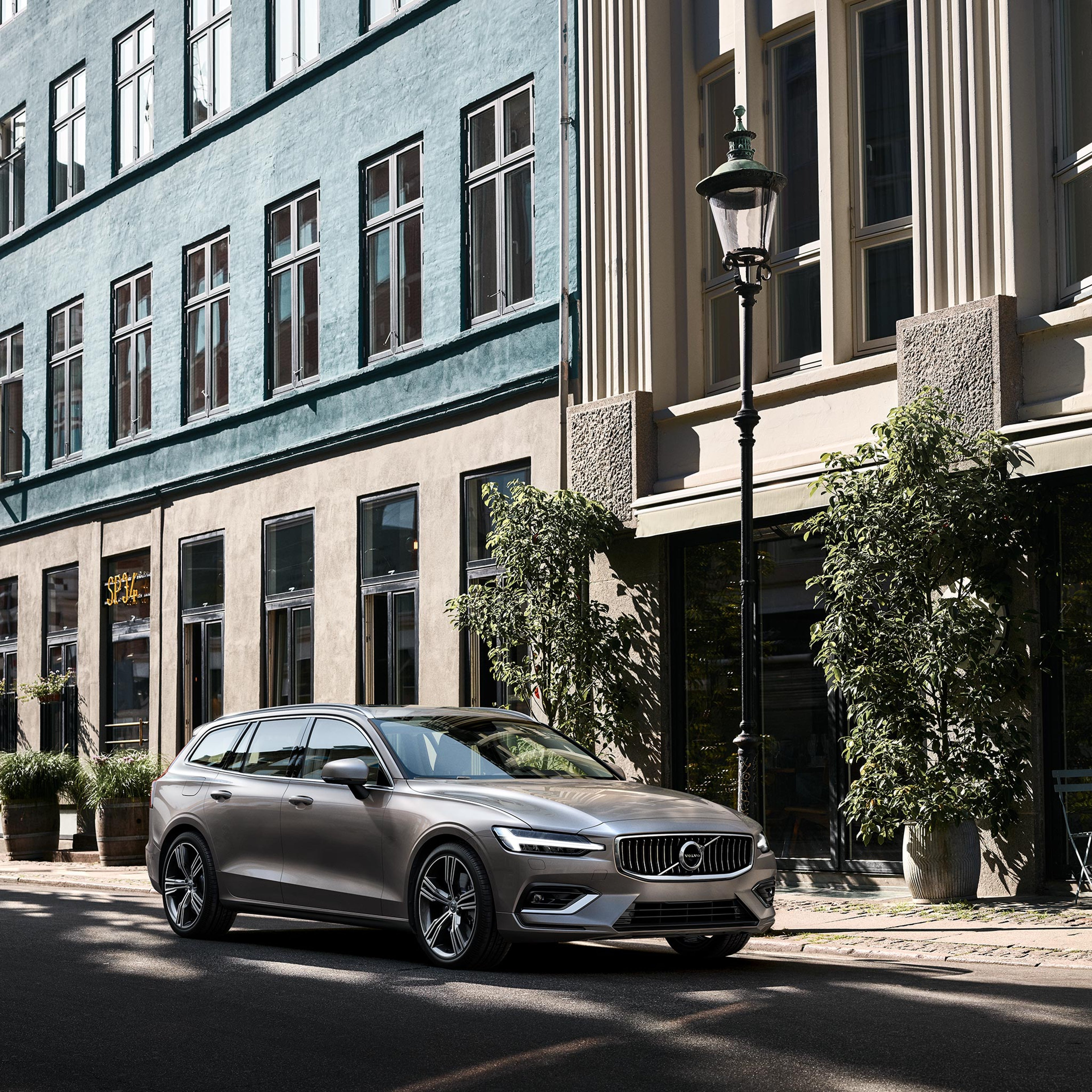 Katukahvilan eteen parkkeerattu Pebble Grey -värinen Volvo V60 lataushybridiauto.