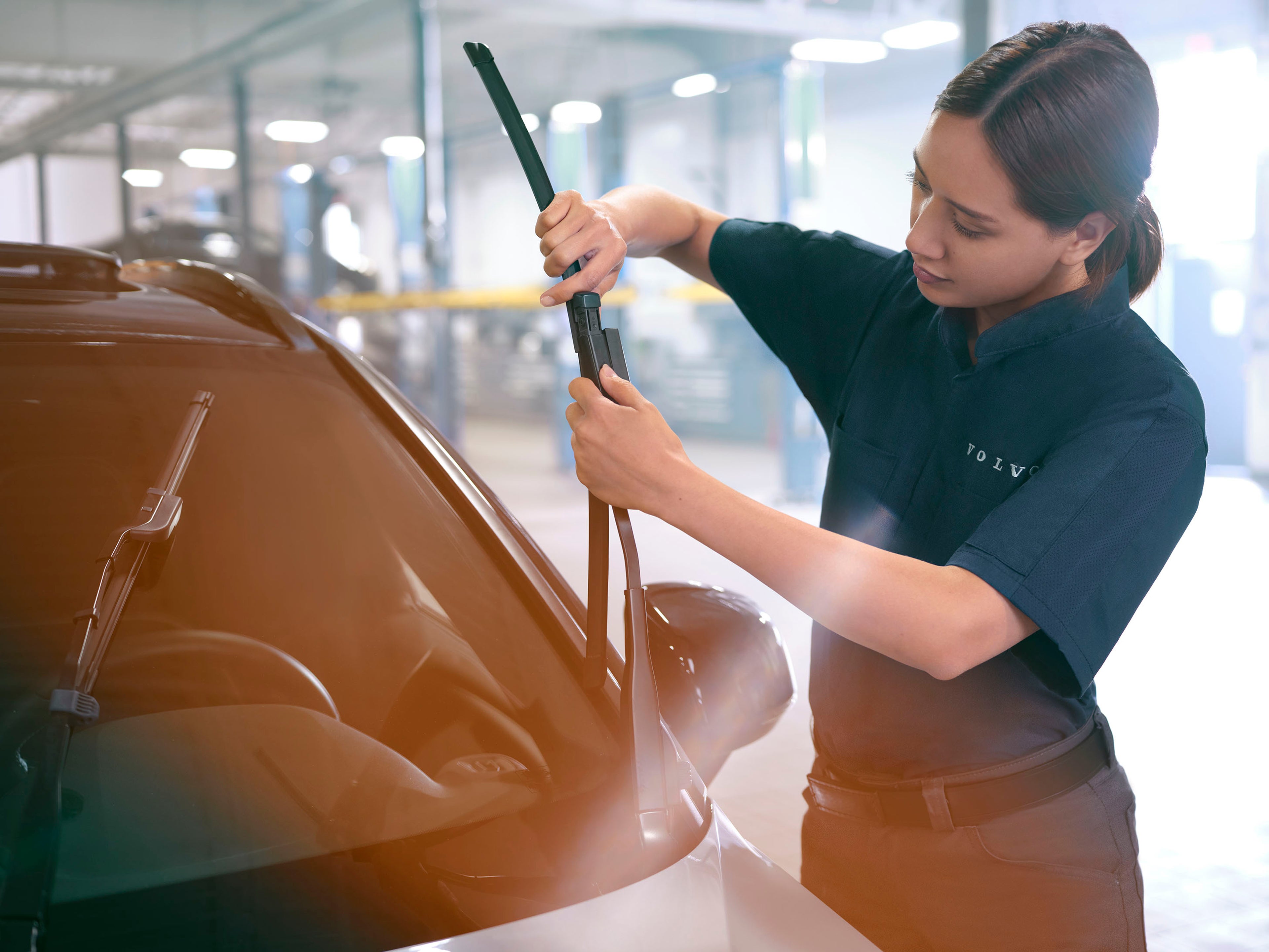 Een vrouwelijke Volvo monteur vervangt de ruitenwissers van een auto in een garage.