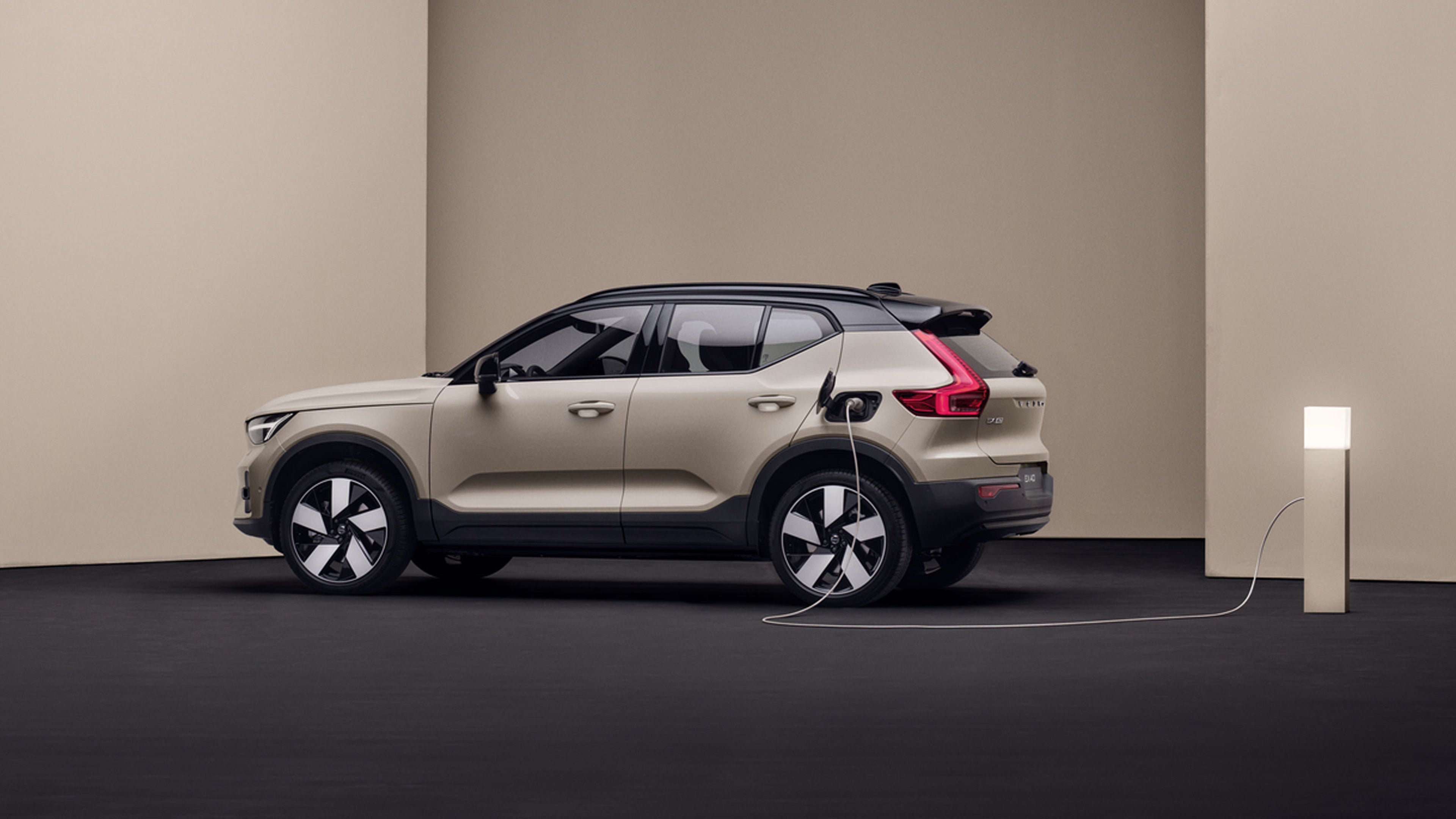 Vue latérale d’un Volvo EX40 beige branché à une borne de recharge dans un décor minimaliste