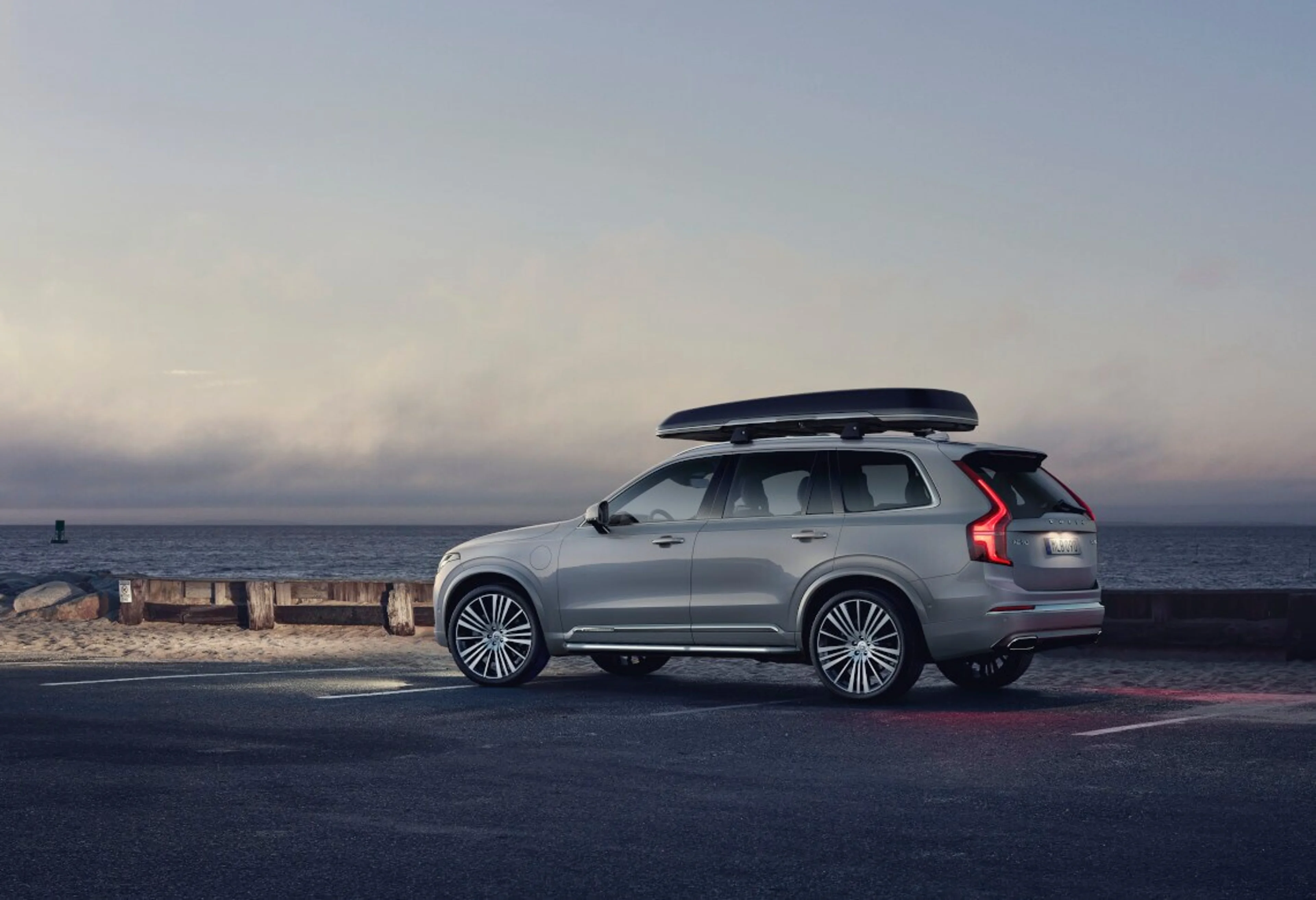 Der Volvo XC90 Inscription in Birch Light mit Dachbox steht am Meer
