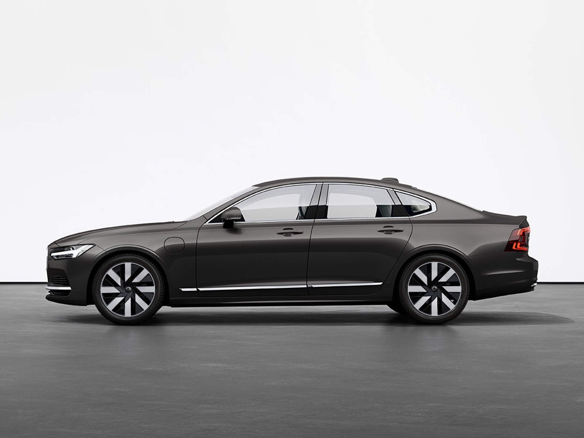 A black Volvo S90 Recharge standing still on grey floor in a studio.