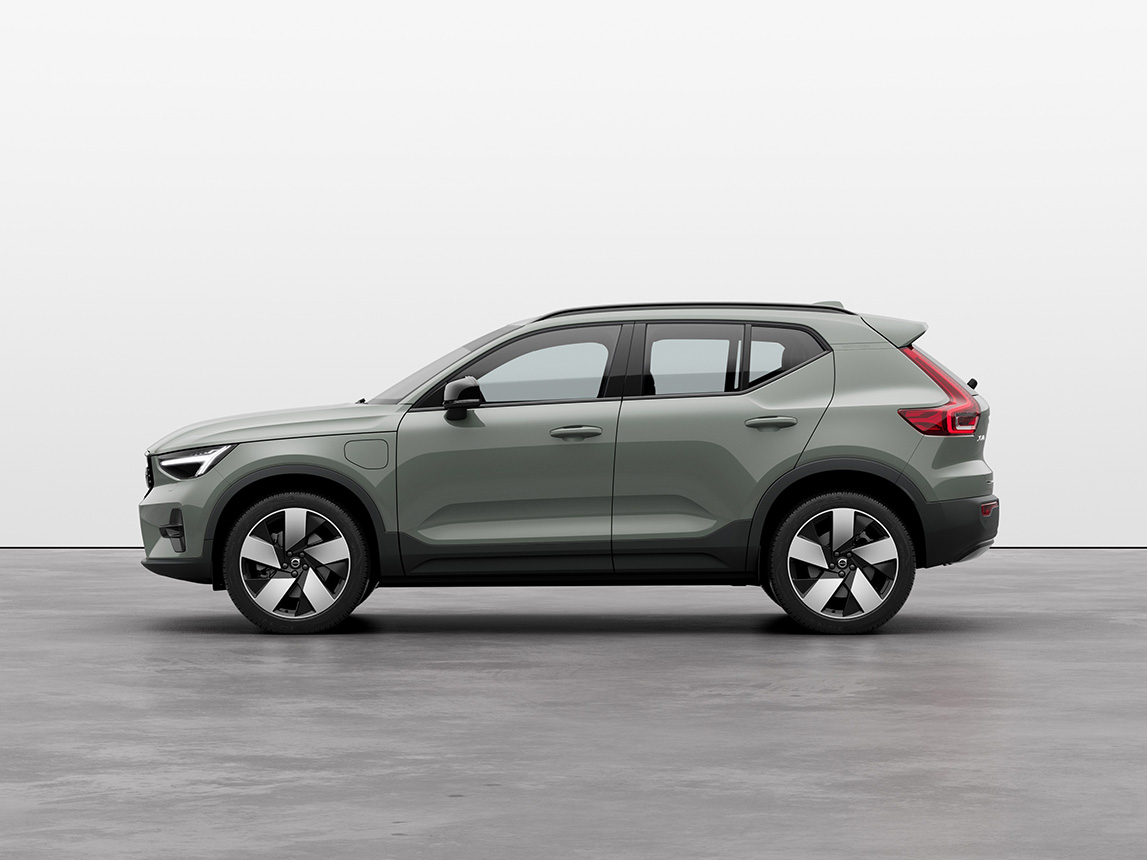 A green Volvo XC40 Recharge plug-in hybrid SUV standing still on grey floor in a studio
