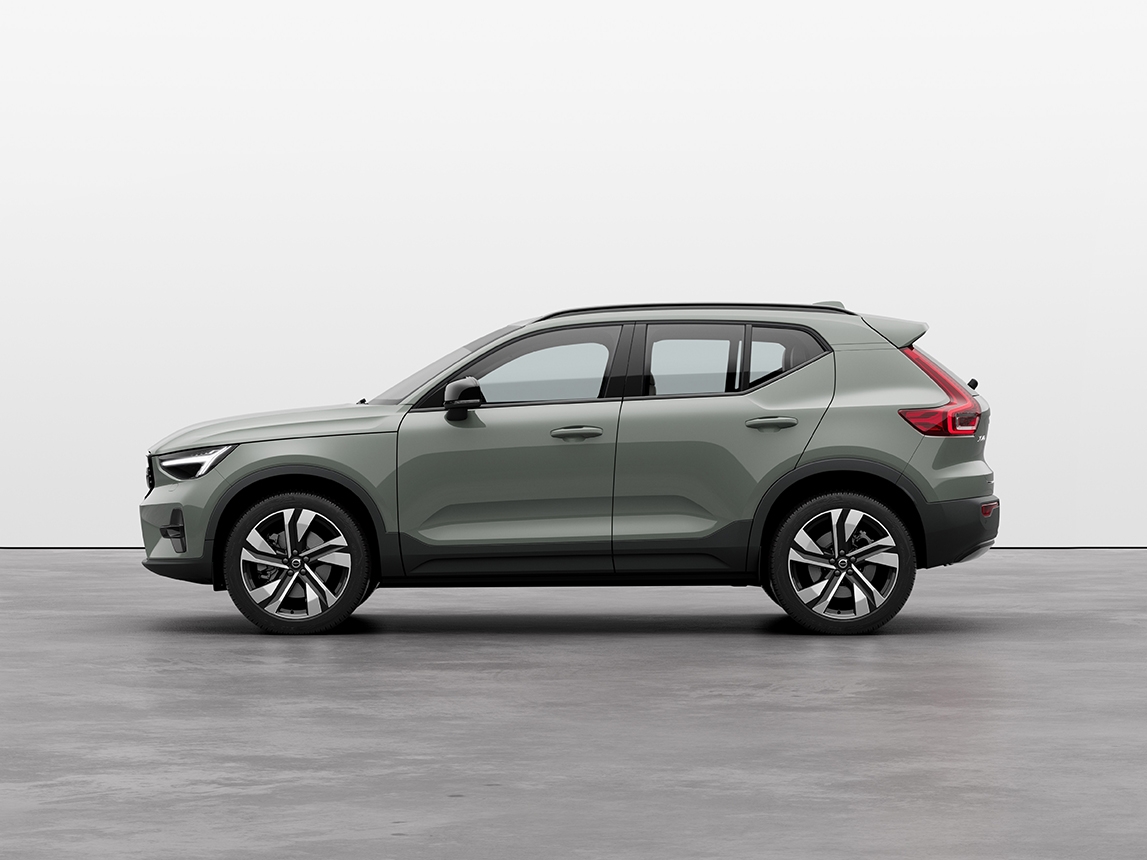 A sage green Volvo XC40 compact SUV standing still on grey floor in a studio