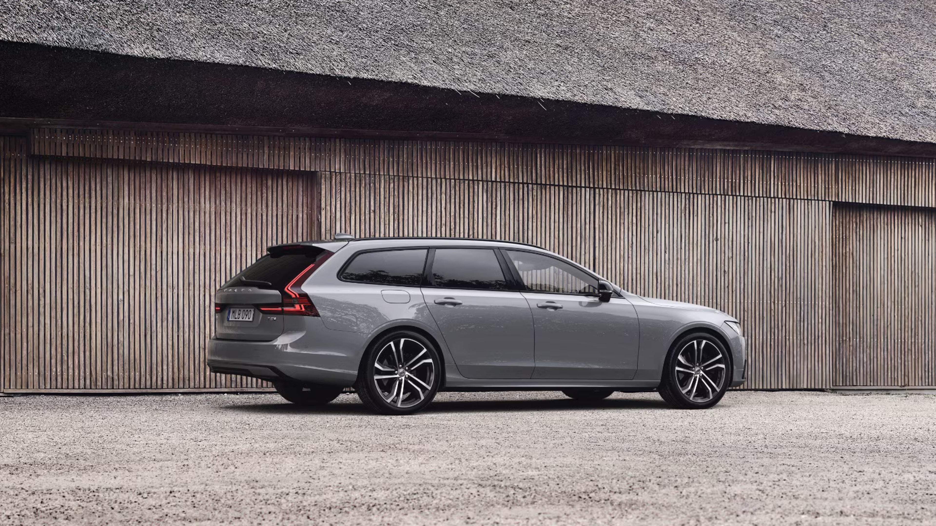Side view of V90 plug-in hybrid parked beside wooden building with a thatched roof