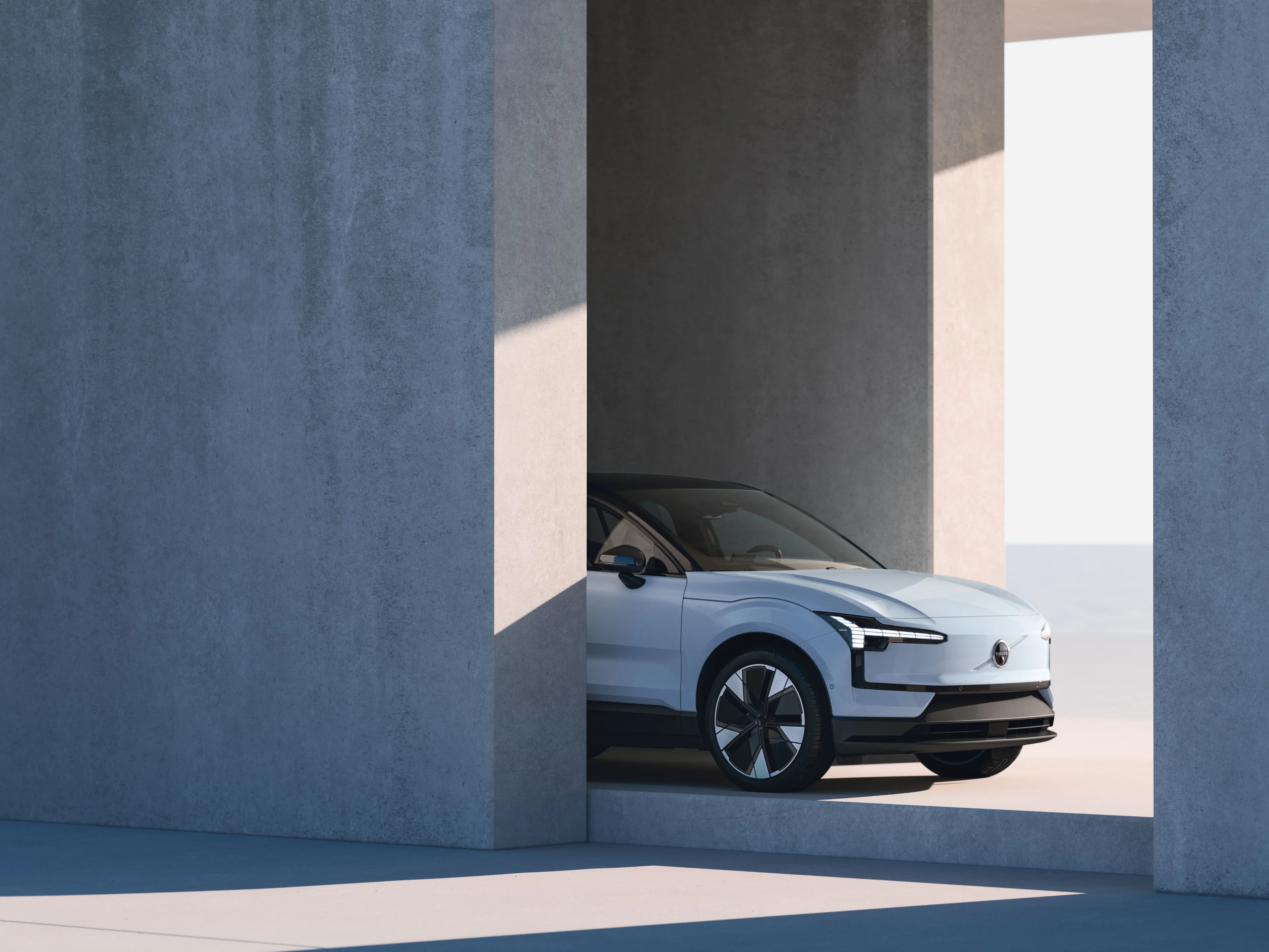 Die Vorderseite und vordere rechte Seite eines Volvo EX30, die durch eine Lücke in einer Betonstruktur sichtbar ist.