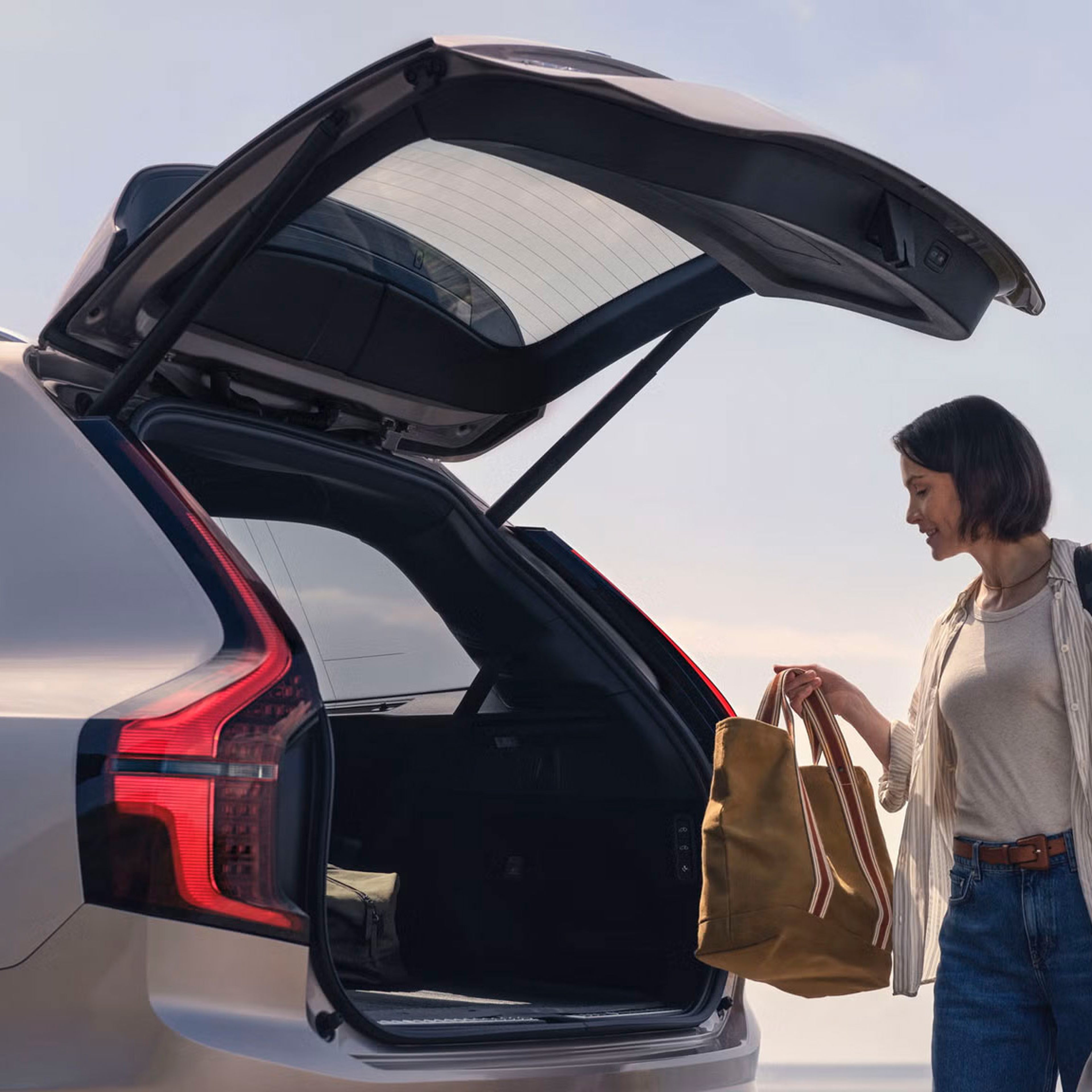 Close up of XC90 with the boot hatch open as someone loads bags into the rear