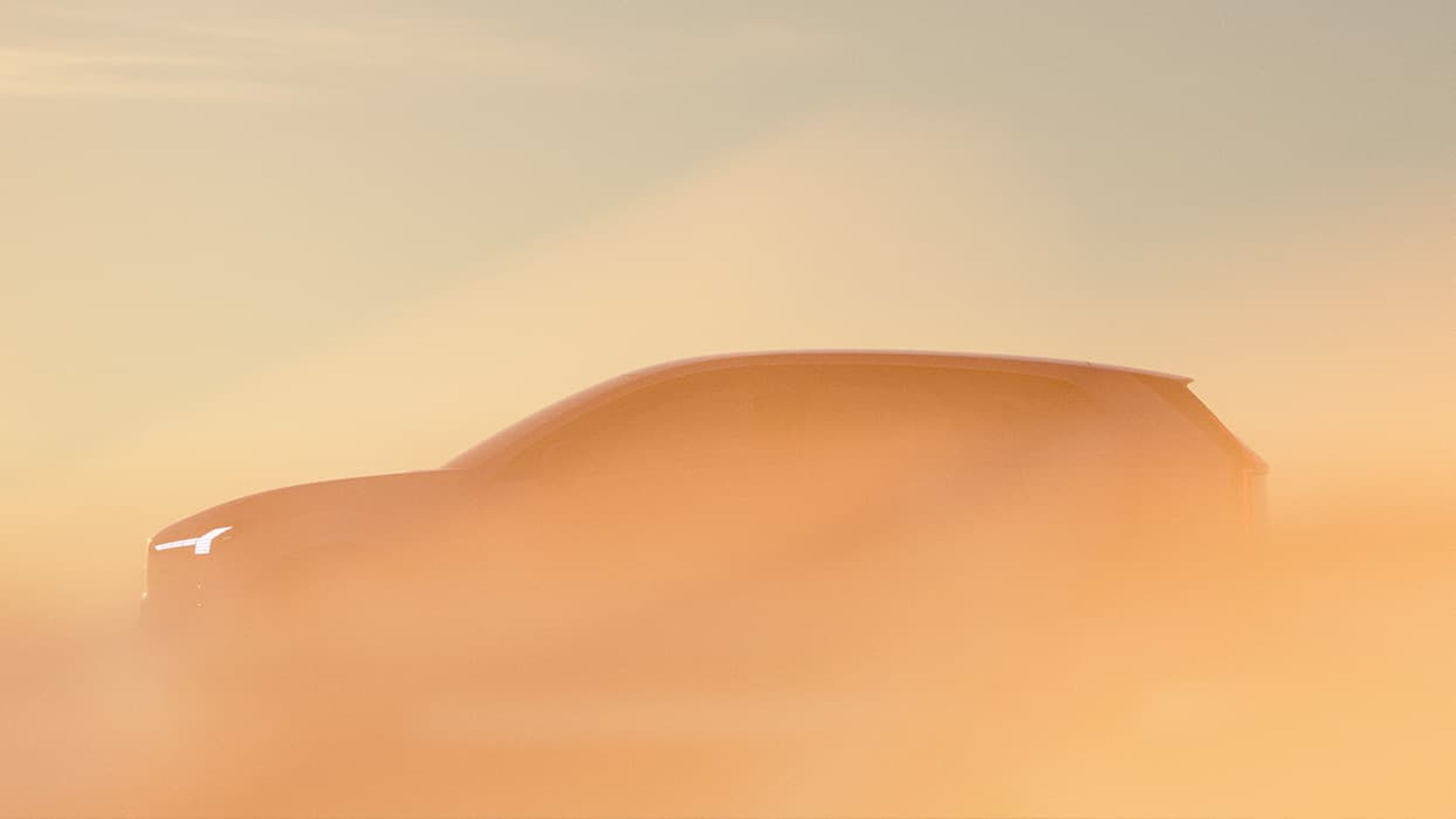 Silhouette d'une Volvo EX60 enveloppé dans un épais brouillard orangé au lever du soleil, avec le phare Marteau de Thor allumé.