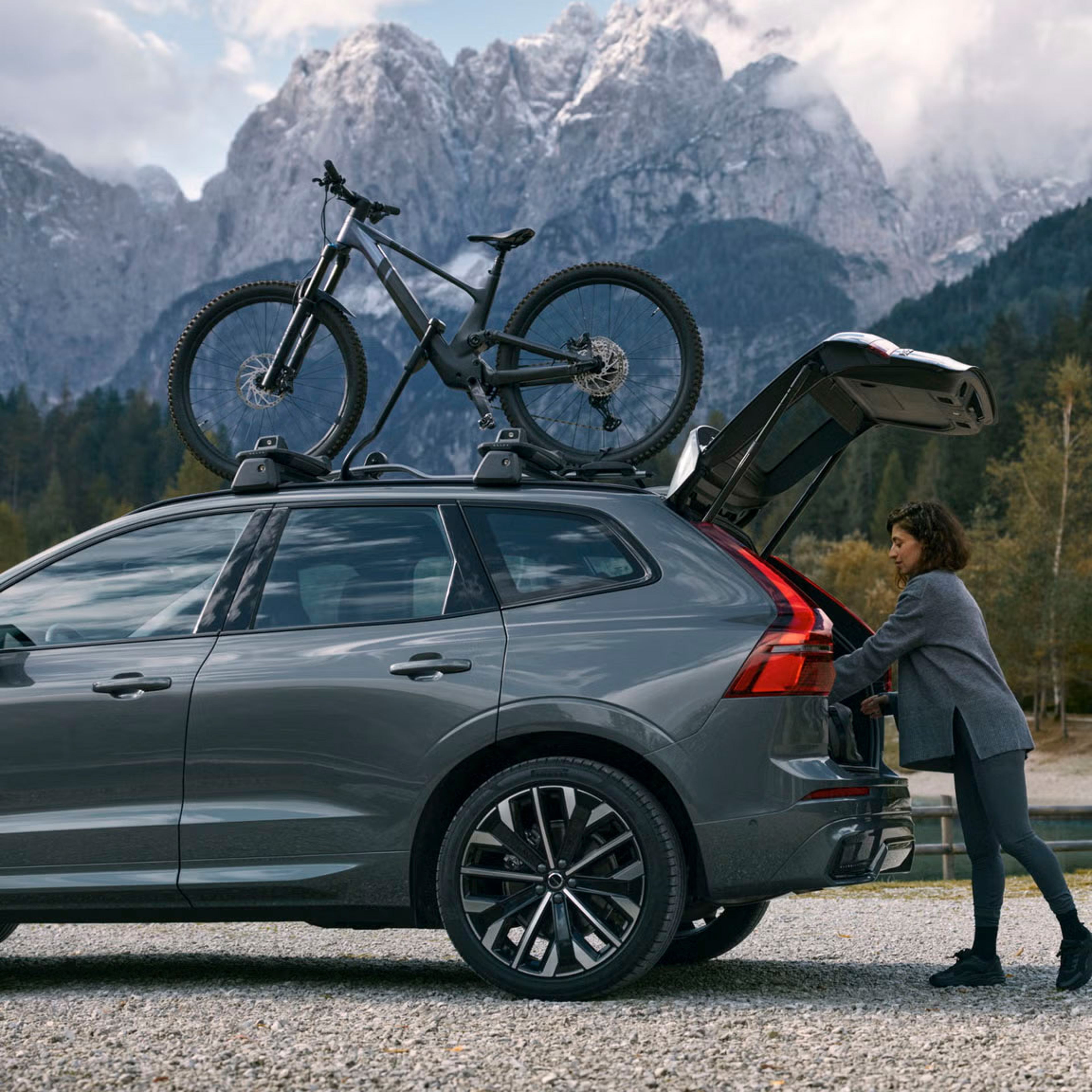 Side view of rear half of XC60 with a bike on the roof and someone loading bags into the boot