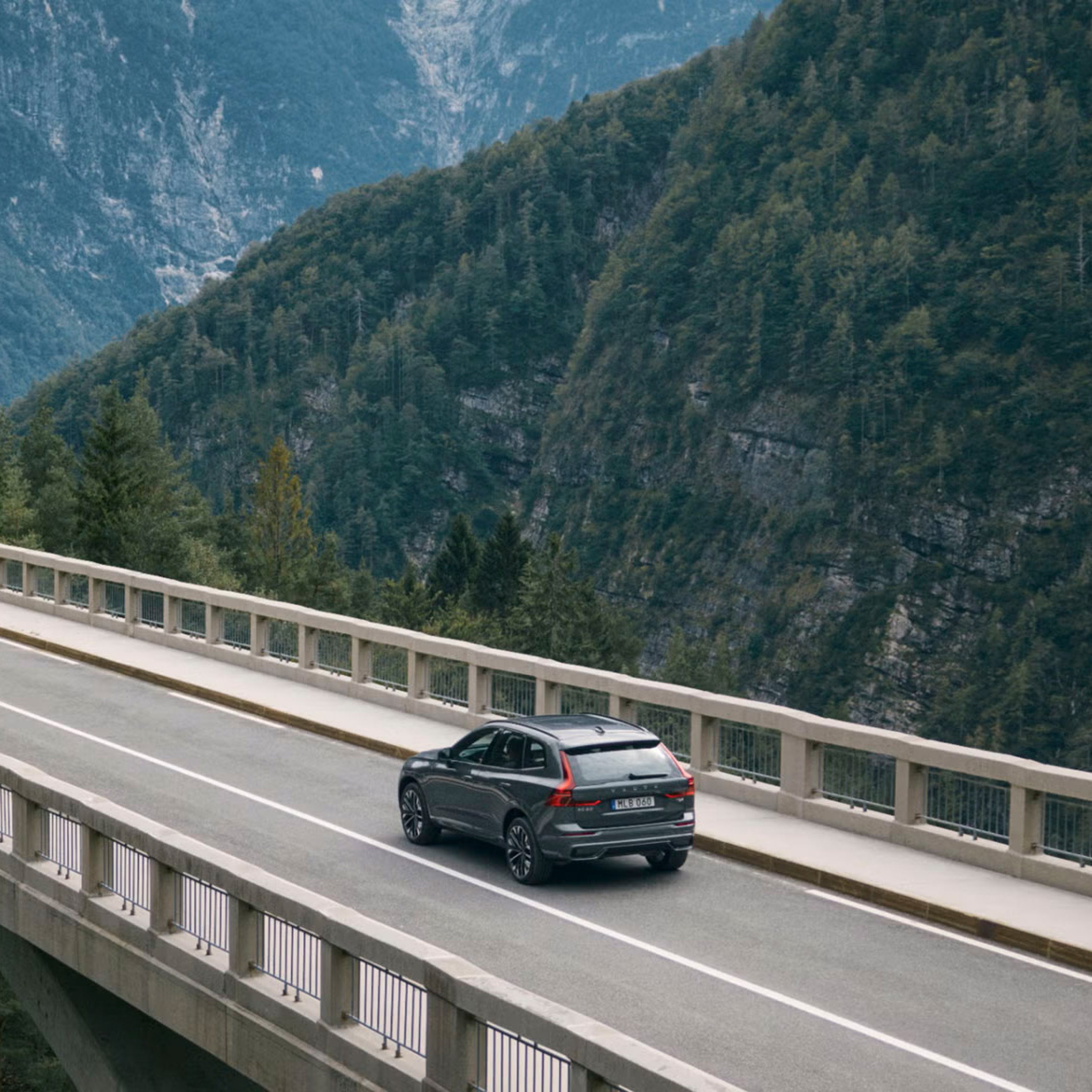 XC60 driving over a bridge beside a picturesque mountainous landscape