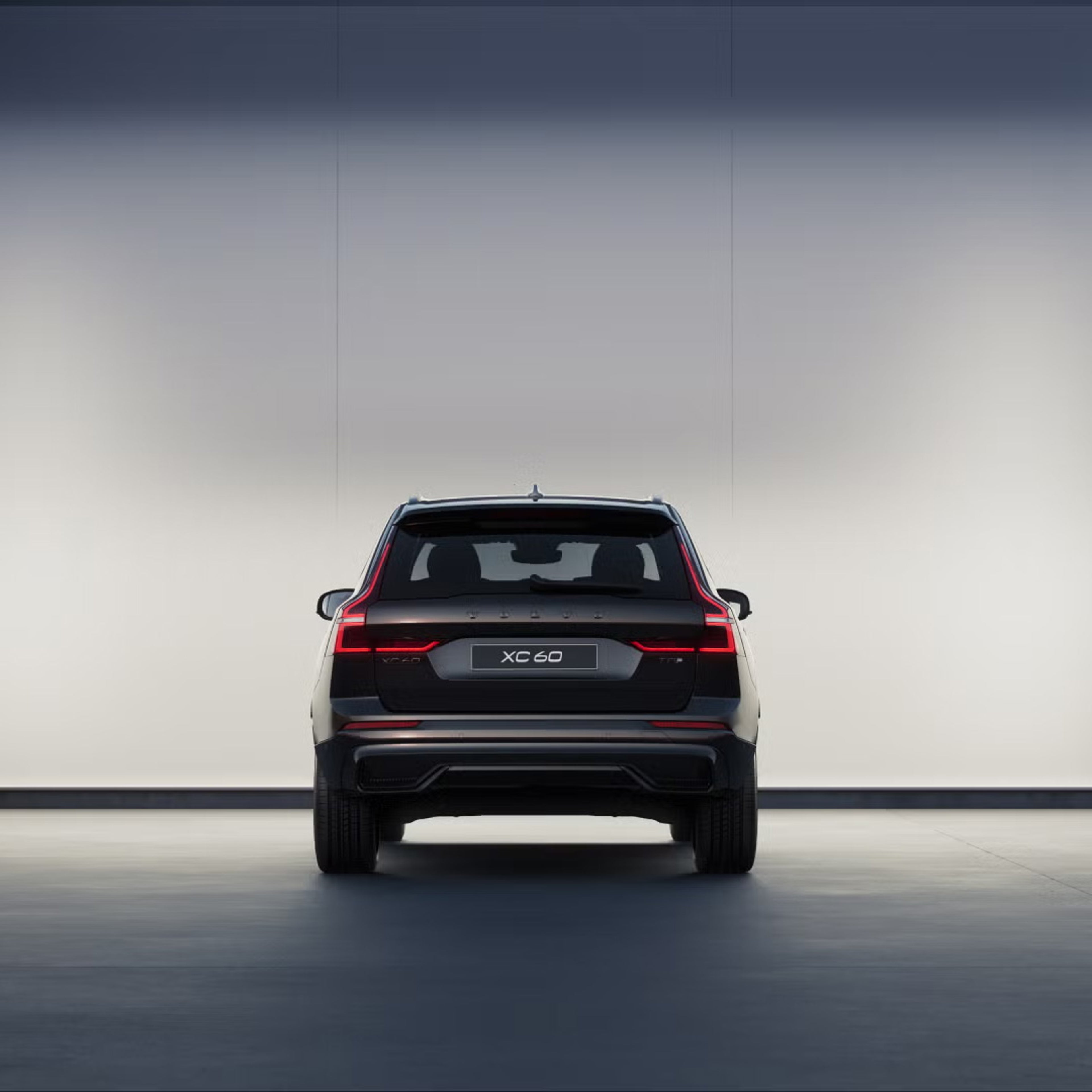 Rear view of XC60 plug-in hybrid black edition in front of softly lit wall