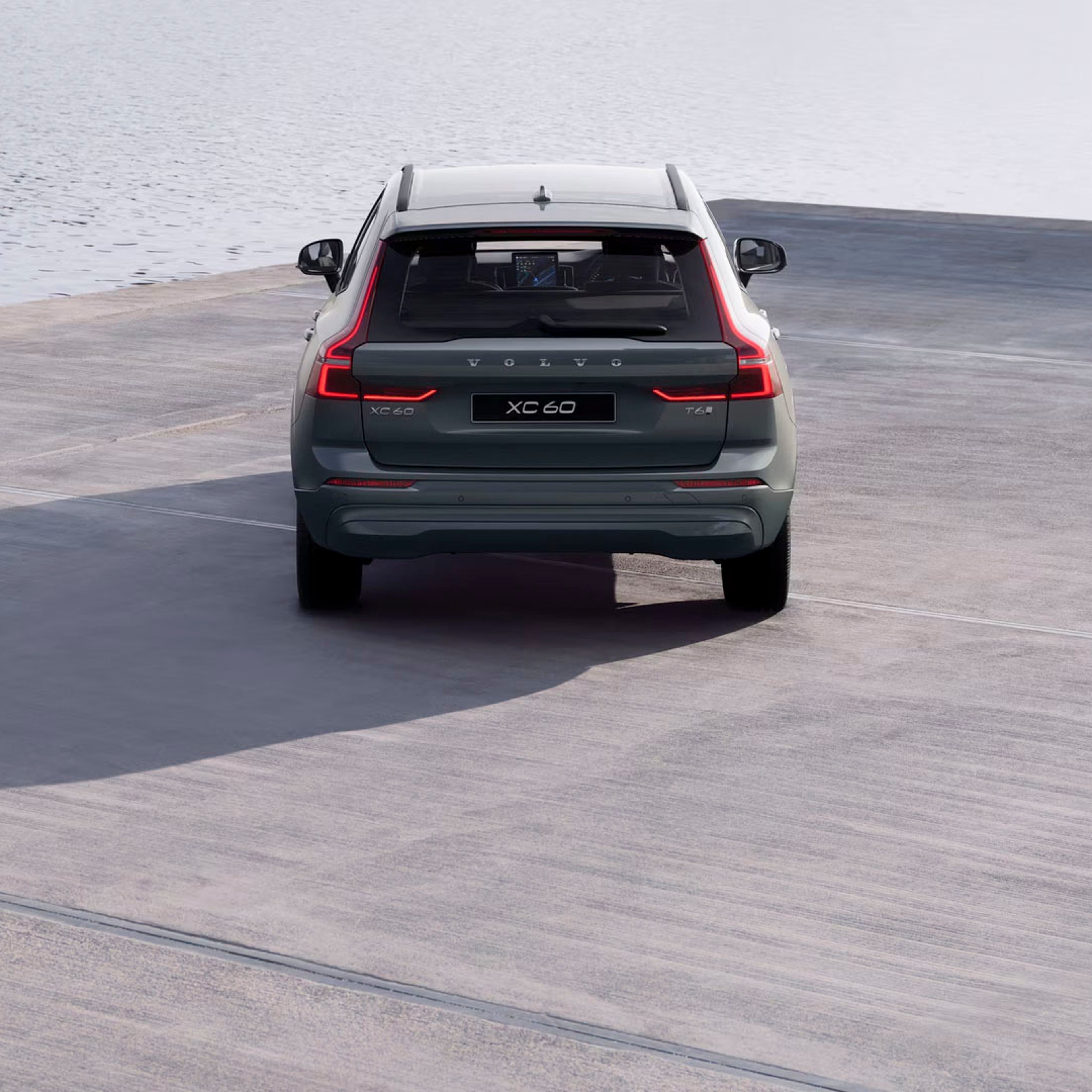 Rear view of an XC60 parked on a grey riverbank facing a lightly rippled body of water
