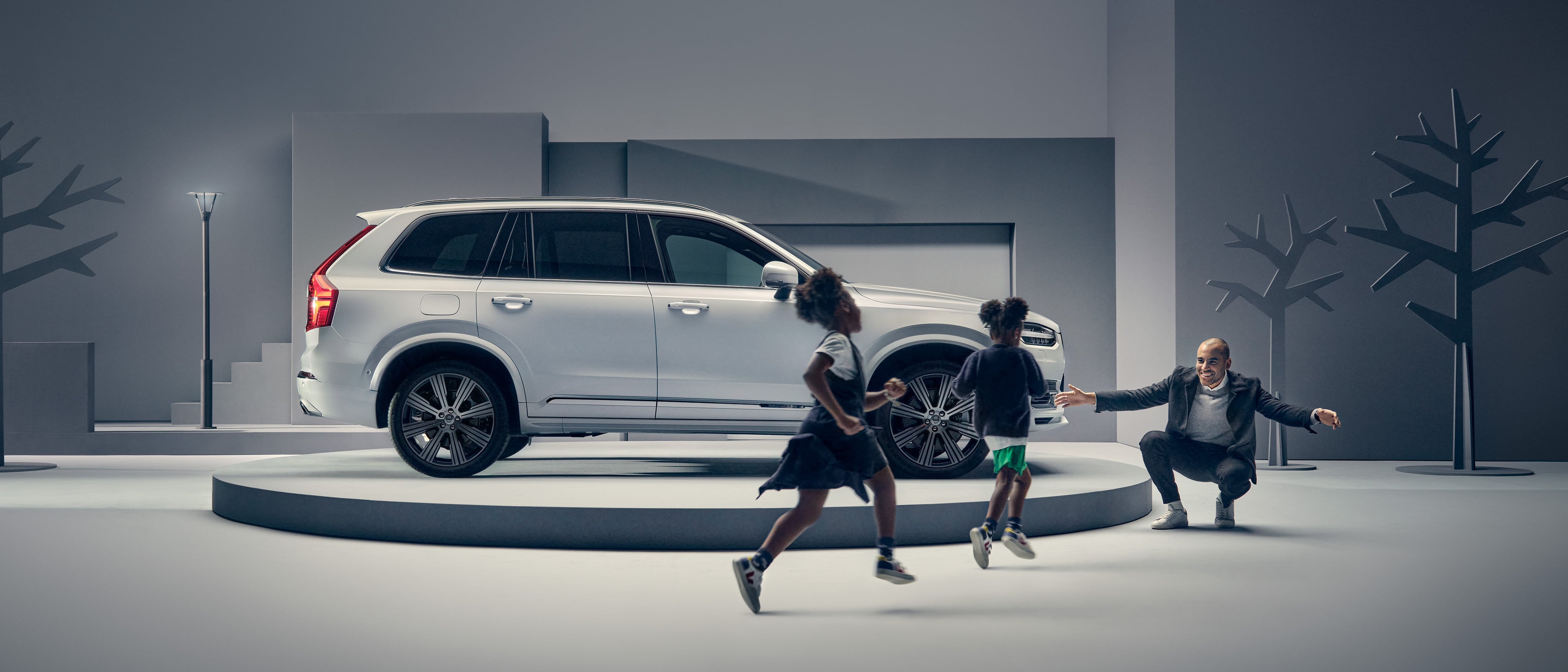 Мужчина машет двум детям, стоя перед автомобилем Volvo на подиуме.