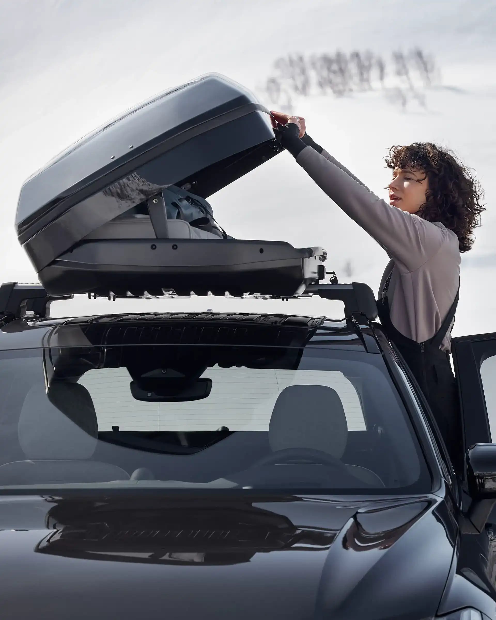 Cestovatel otevírající střešní box na voze Volvo XC60 v zasněženém terénu.