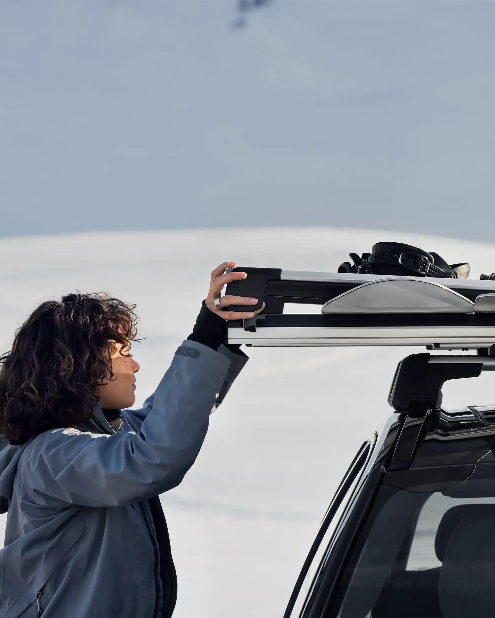 Zimní cestovatelka vyjímající lyžařské vybavení z nosiče lyží Volvo.
