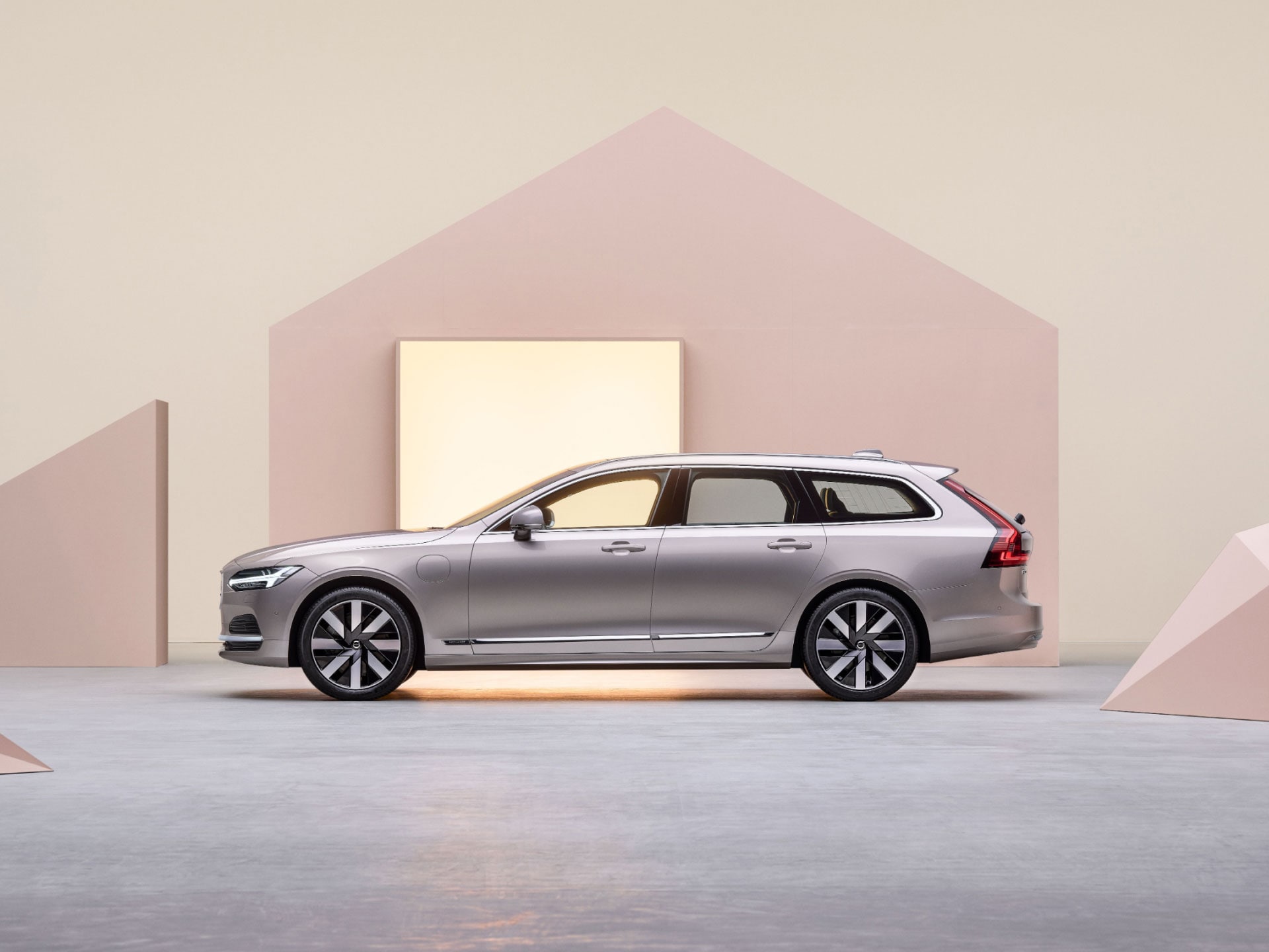 A wide-angle view of the side of a plug-in hybrid Volvo estate car plugged into a charger.