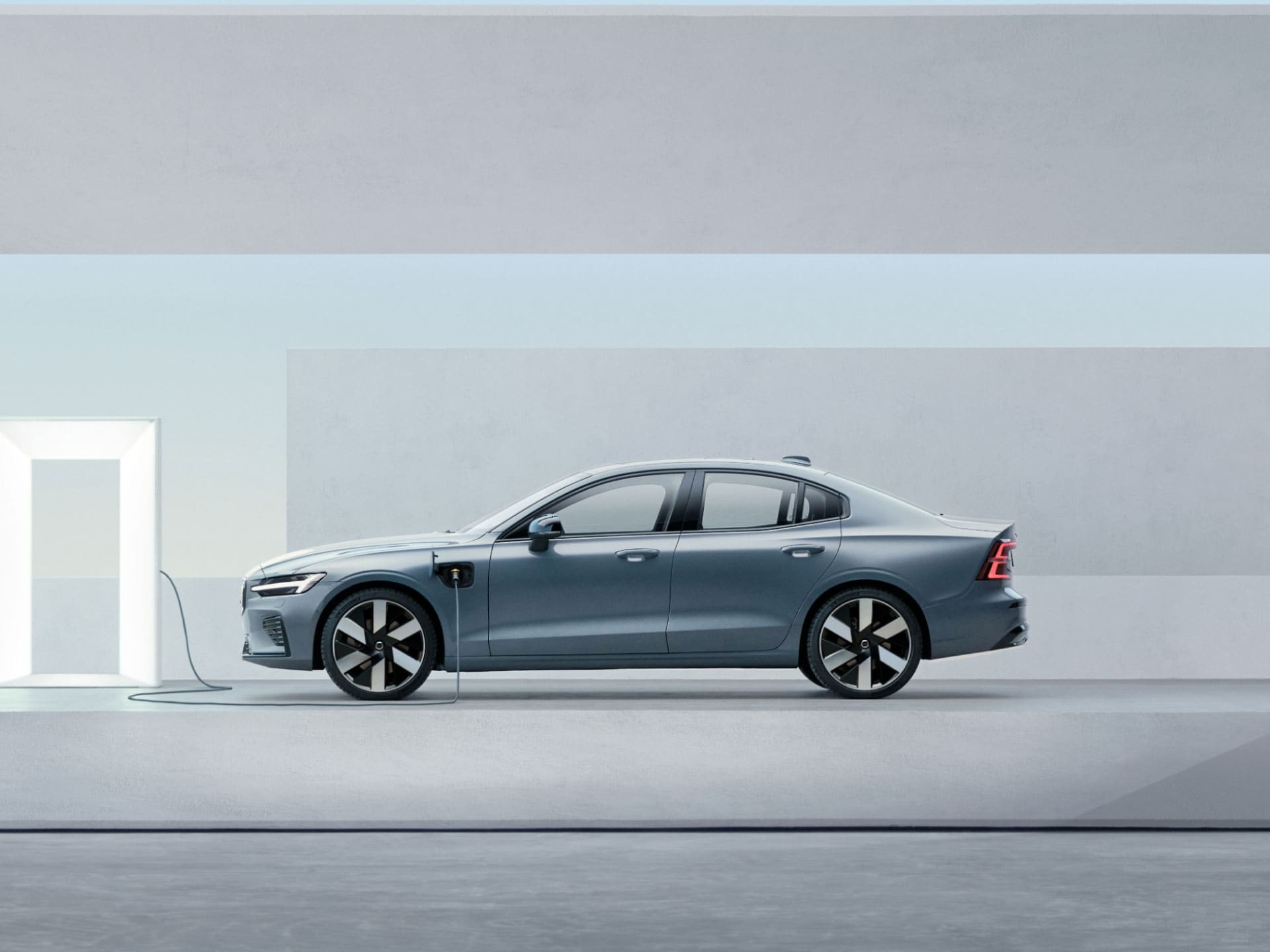 A wide-angle view of the side of a Volvo plug-in hybrid sedan car plugged into a charger.