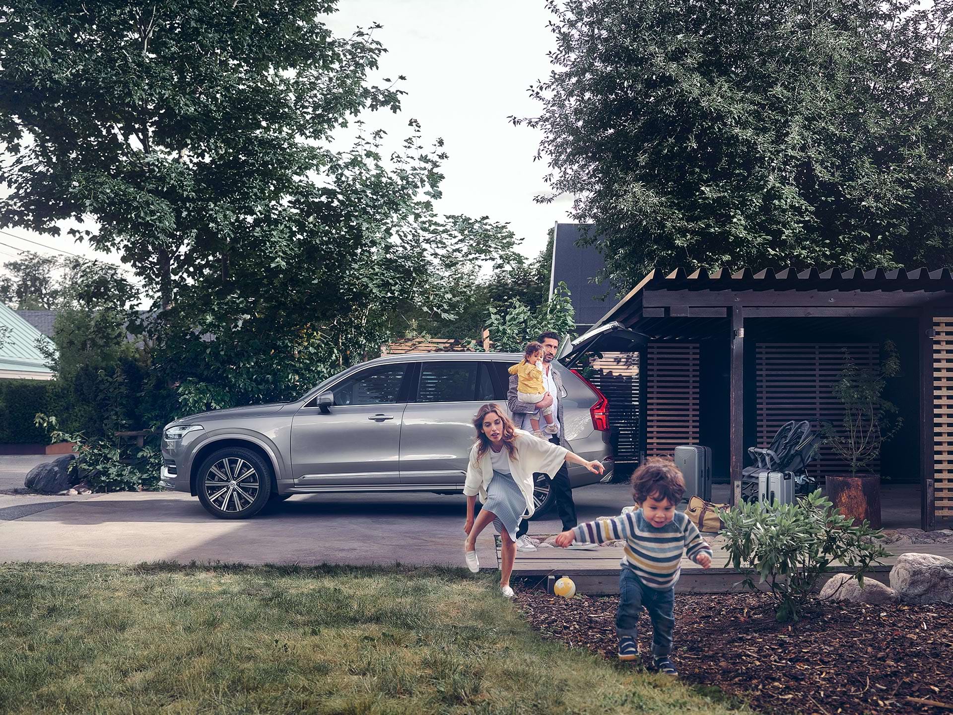 As a suburban family prepares for a trip in their Volvo SUV, a child runs across the yard chased by his mother.