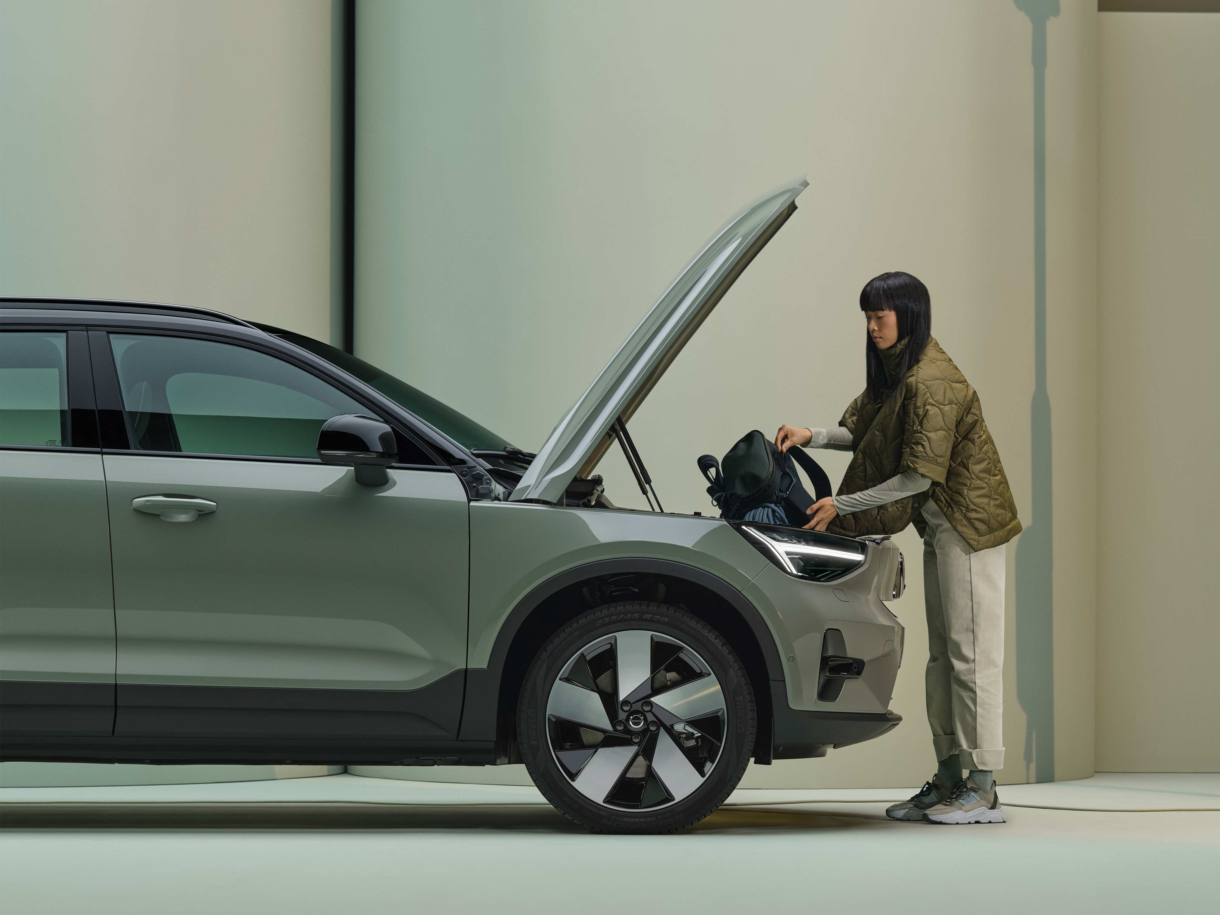 A woman places a small black bag in the front cargo compartment of her fully electric Volvo SUV.