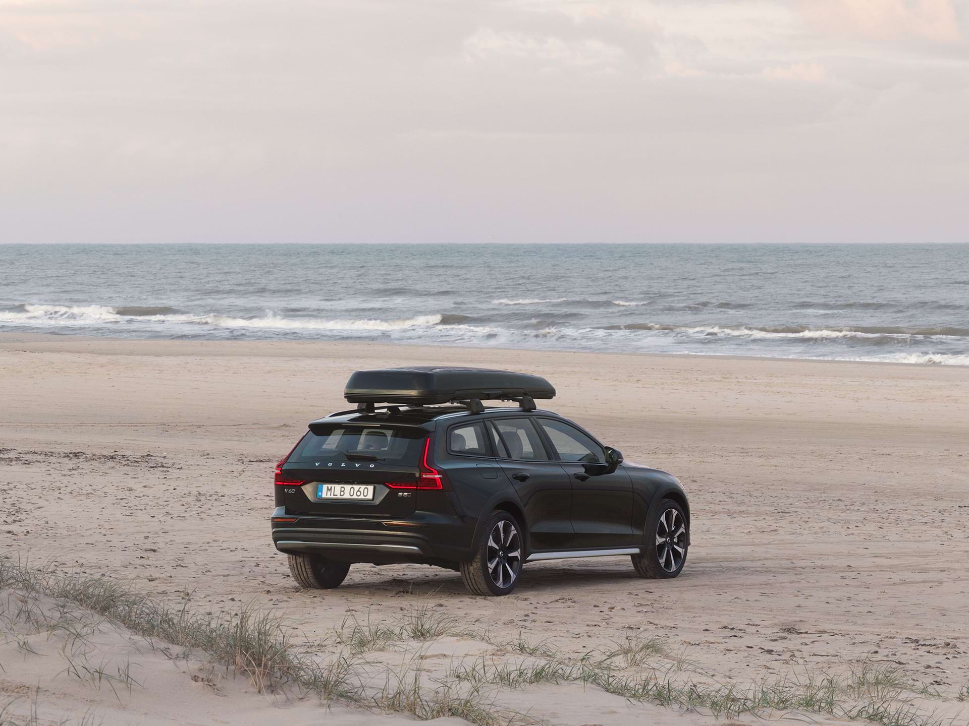 Een Volvo estate met dakkoffer staat geparkeerd op een zandstrand.