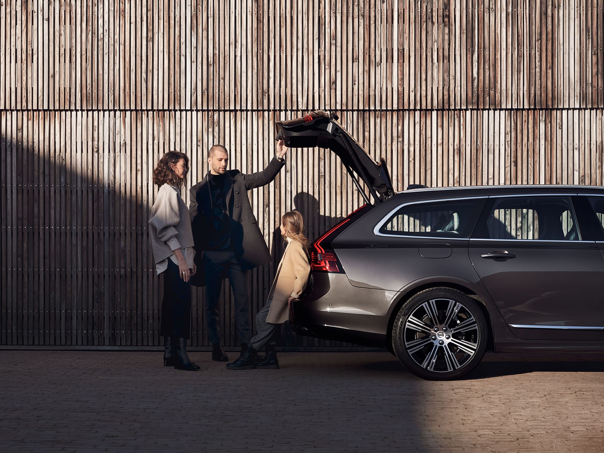 Een man, vrouw en kind staan dicht bij een Volvo estate met de achterklep open terwijl de man zijn hand erop legt.