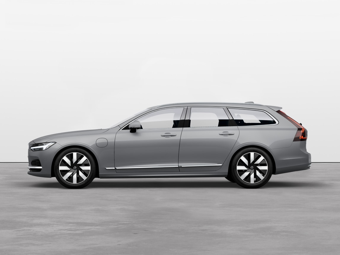A vapour grey Volvo V90 Recharge plug-in hybrid estate standing still on grey floor in a studio.