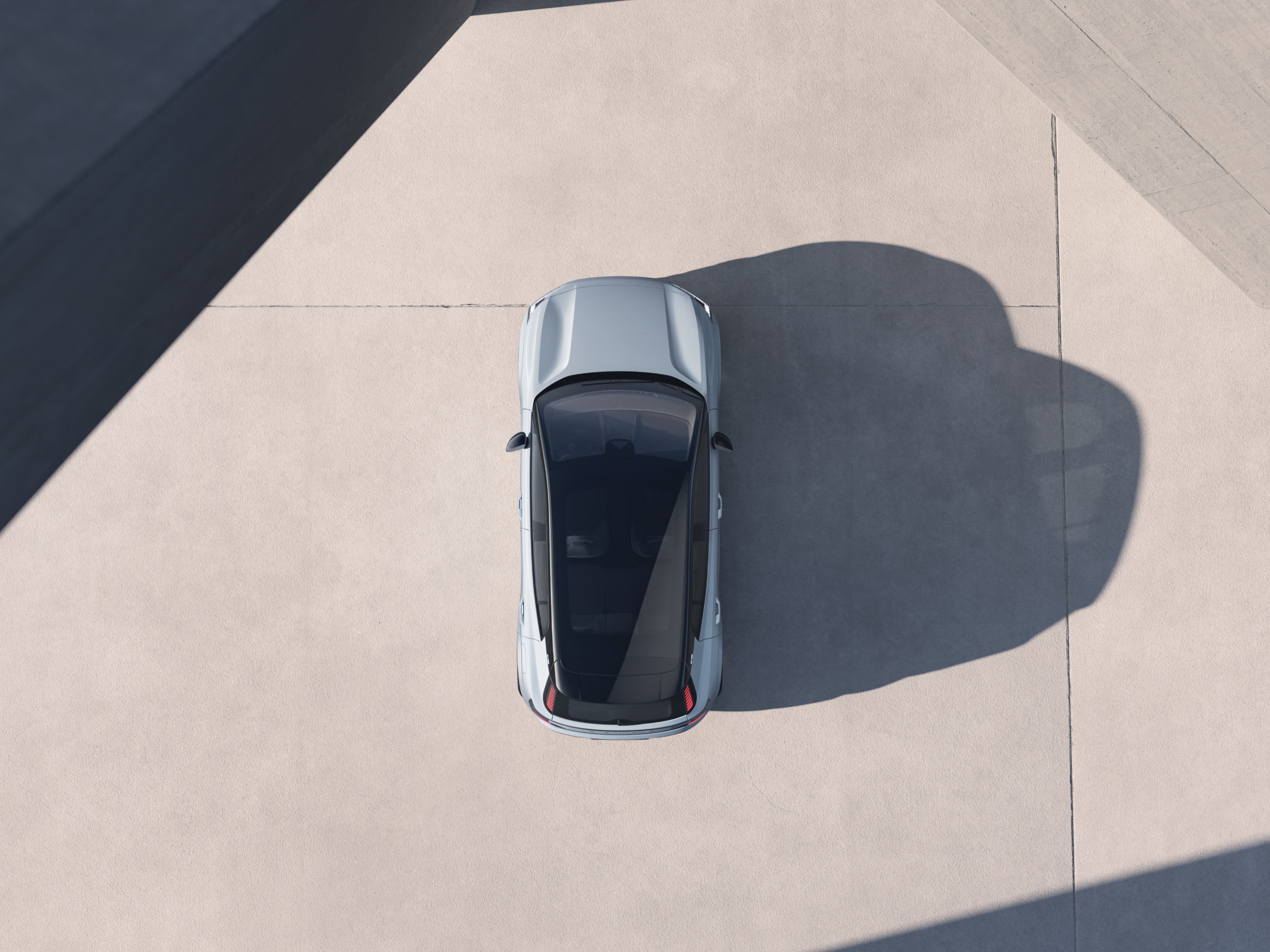 Ein Volvo EX30 aus der Vogelperspektive, der von der Seite angestrahlt wird, so dass er einen langen Schatten wirft.