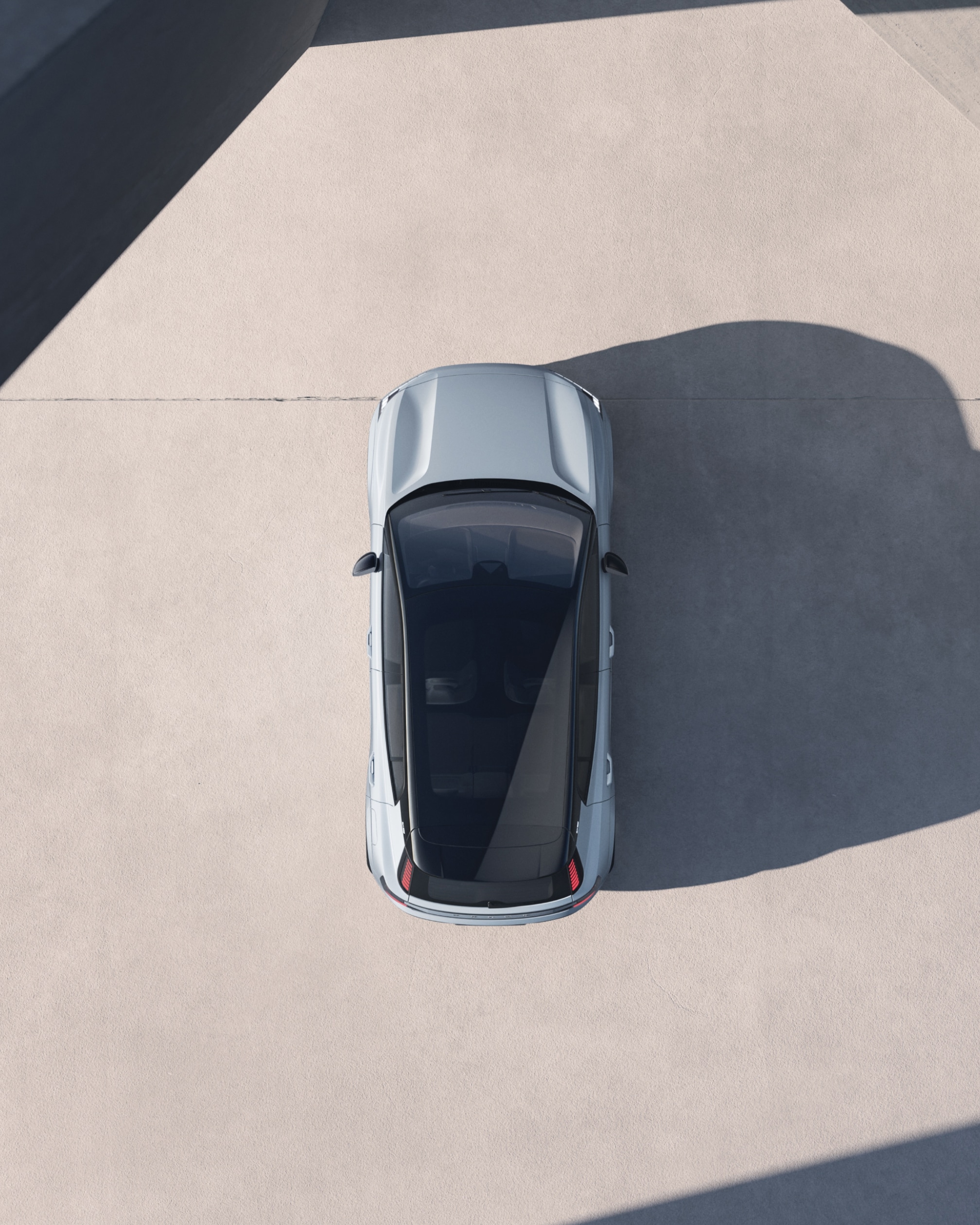 A bird's eye view of a Volvo EX30 that's lit boldly from the side, so it casts a long shadow.