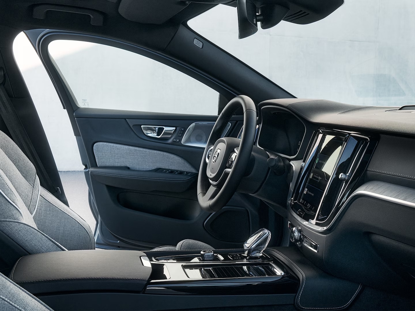 Vista interior del asiento del conductor, el volante, la pantalla de infoentretenimiento, la palanca de cambios de cristal y la puerta del asiento del conductor en el Volvo S60 Recharge híbrido enchufable.