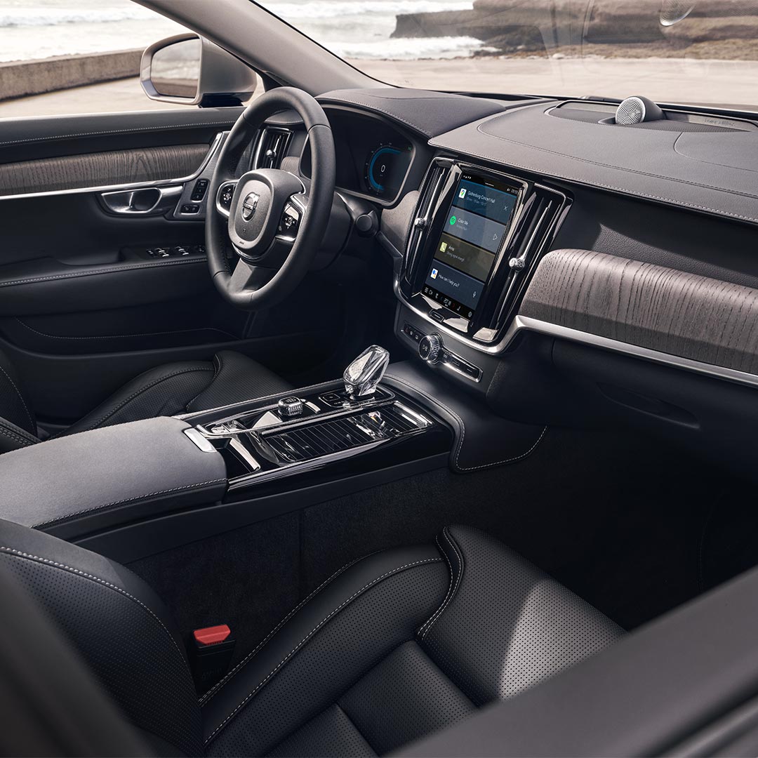 Interieur van een Volvo S90 met bestuurderszetel, stuur en centrale display met aanraakscherm.