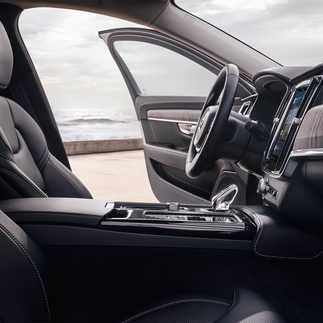 Binnenaanzicht van een Volvo S90 met bestuurderszetel, stuur, versnellingspook en centrale display met aanraakscherm.