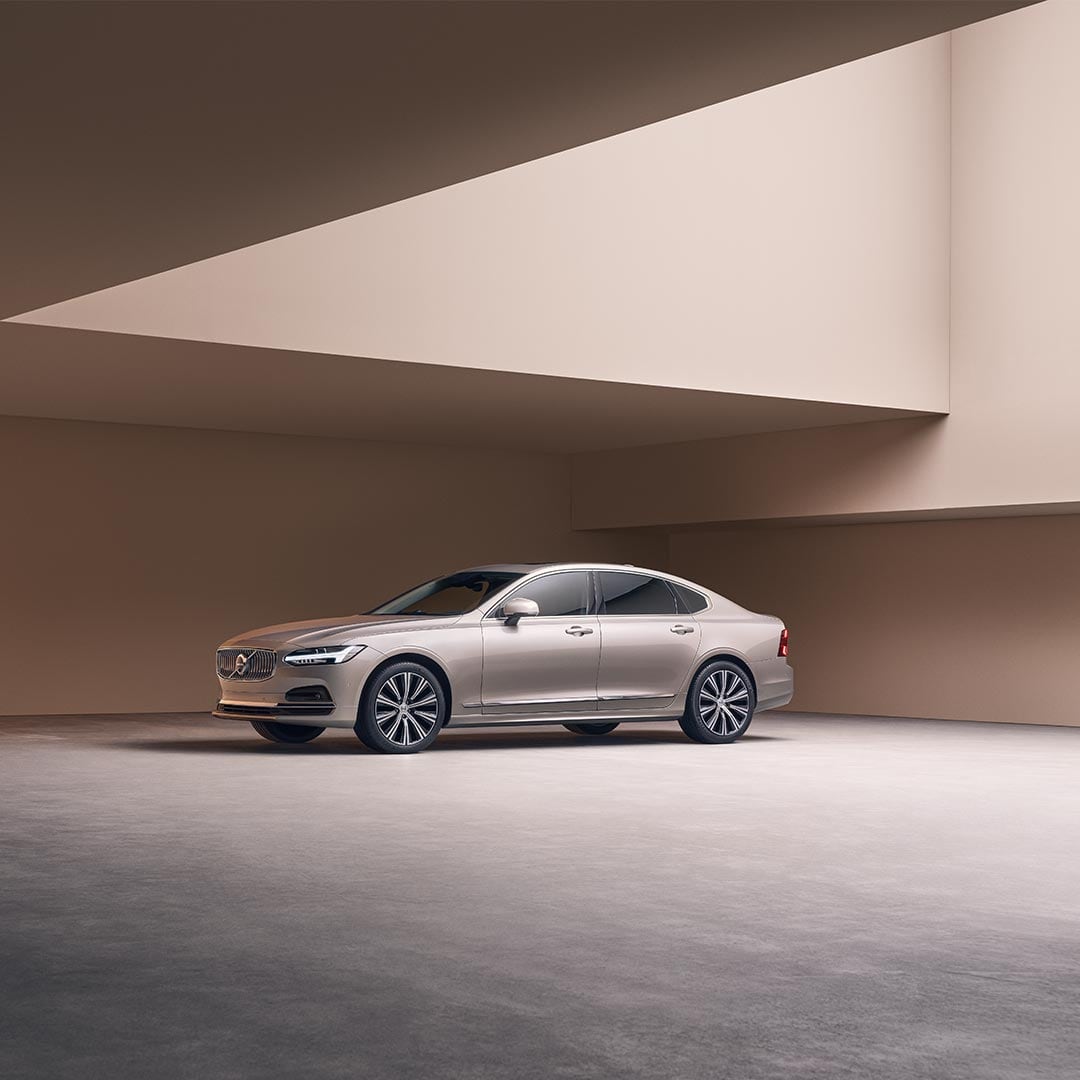 A wide-angle image of the left side and partial view of the front of a Volvo S90 parked in a large concrete structure.