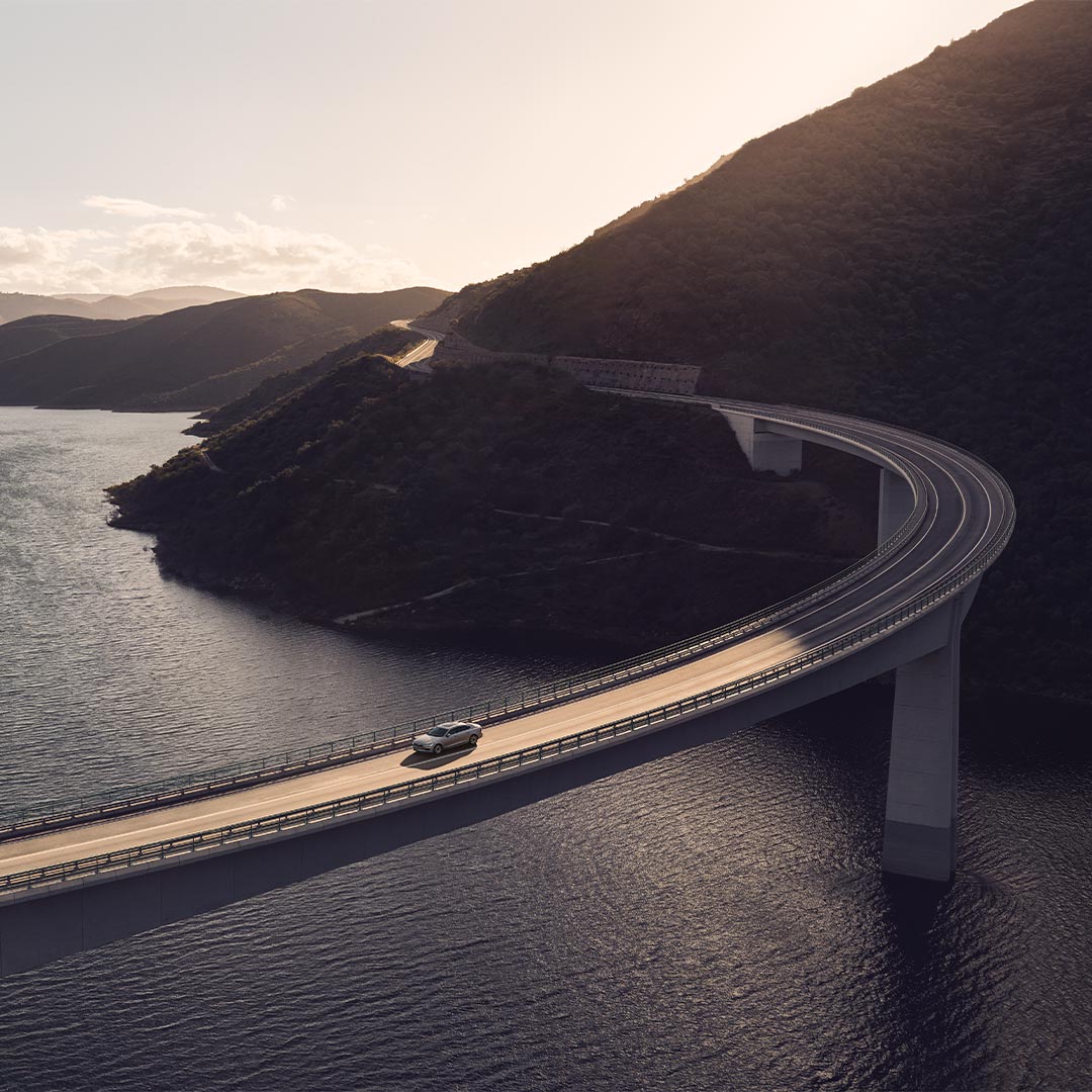A wide-angle image of a Volvo S90 driving over a bridge overlooking a river and mountains.