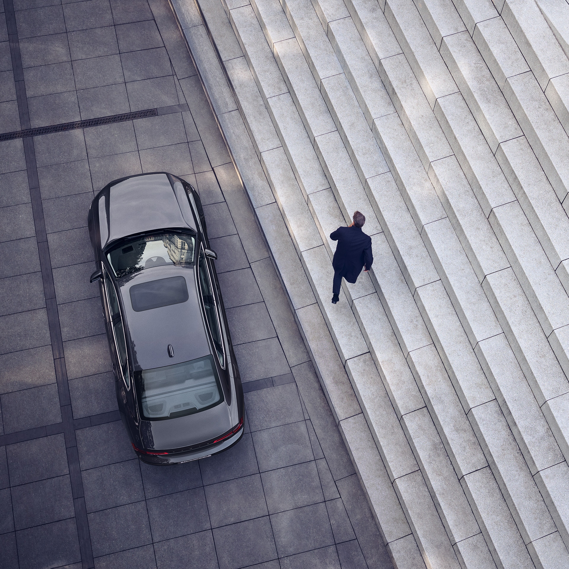 Ein Volvo S90 ist vor einer Treppe geparkt, ein Mann geht vom Auto weg.