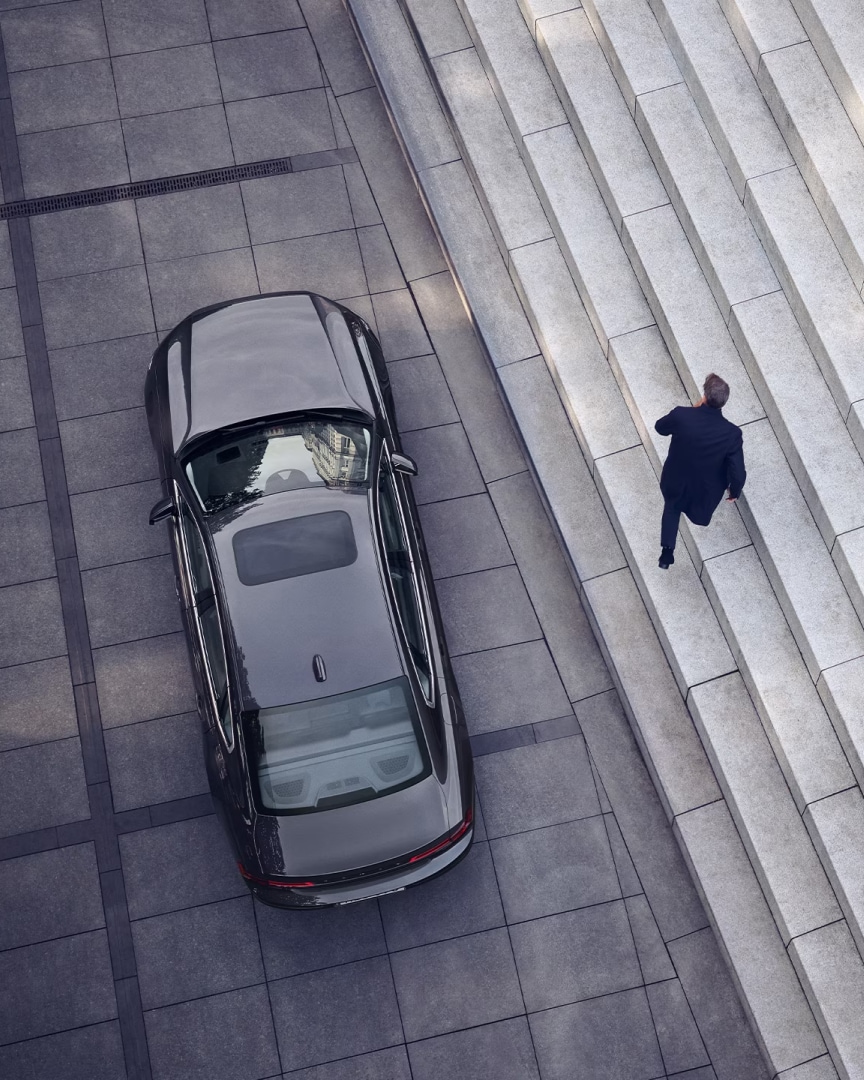 A Volvo S90 is parked in front of a set of stairs, a man walks away from the car.