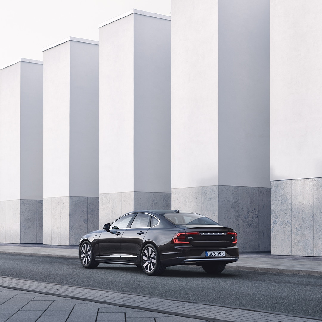 Volvo S90 Recharge с изглед от задната страна пред бетонна стена.