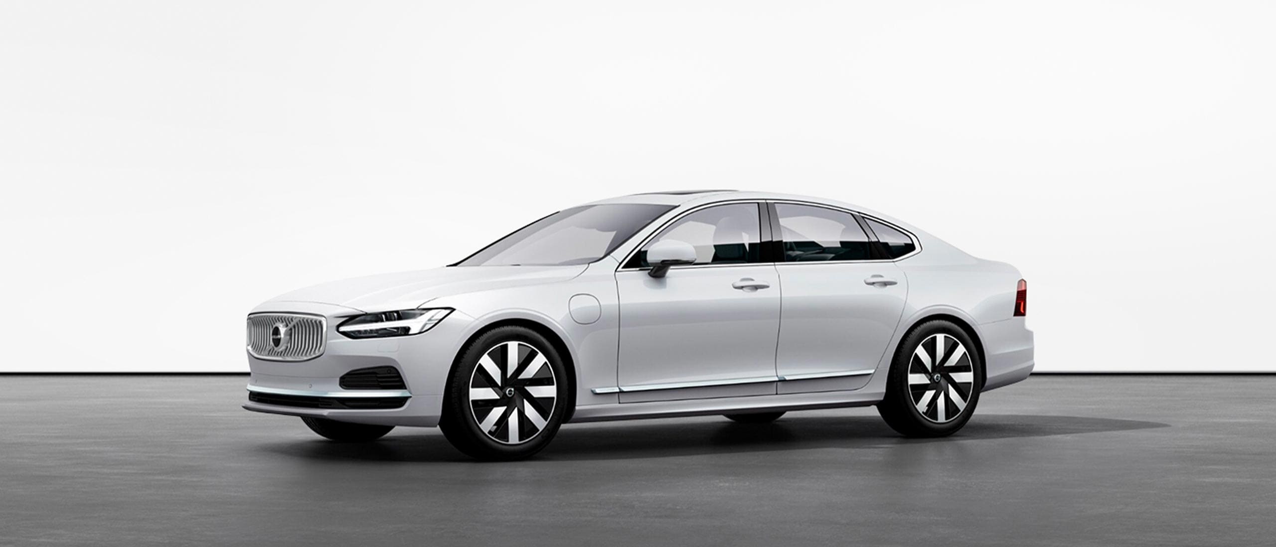 A white Volvo S90 Recharge plug-in hybrid standing still on grey floor in a studio.