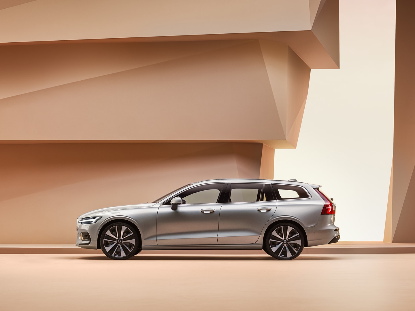 Zijaanzicht van een Volvo S90 die voor een grijze betonnen muur geparkeerd is.