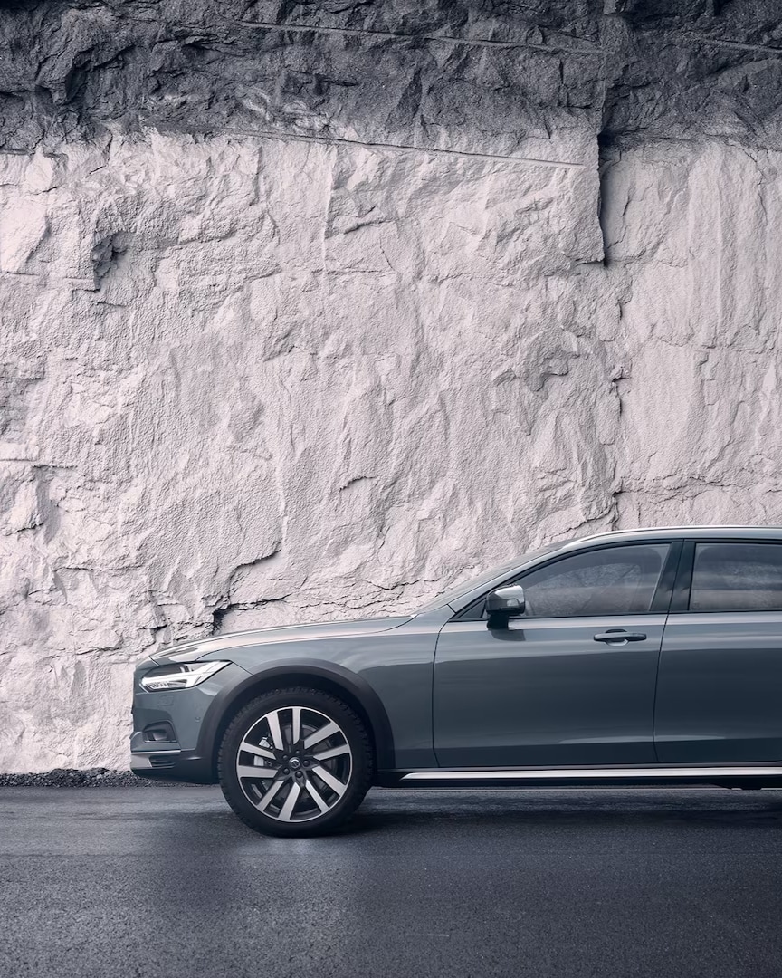 A grey Volvo V90 Cross Country parked against a rock wall.