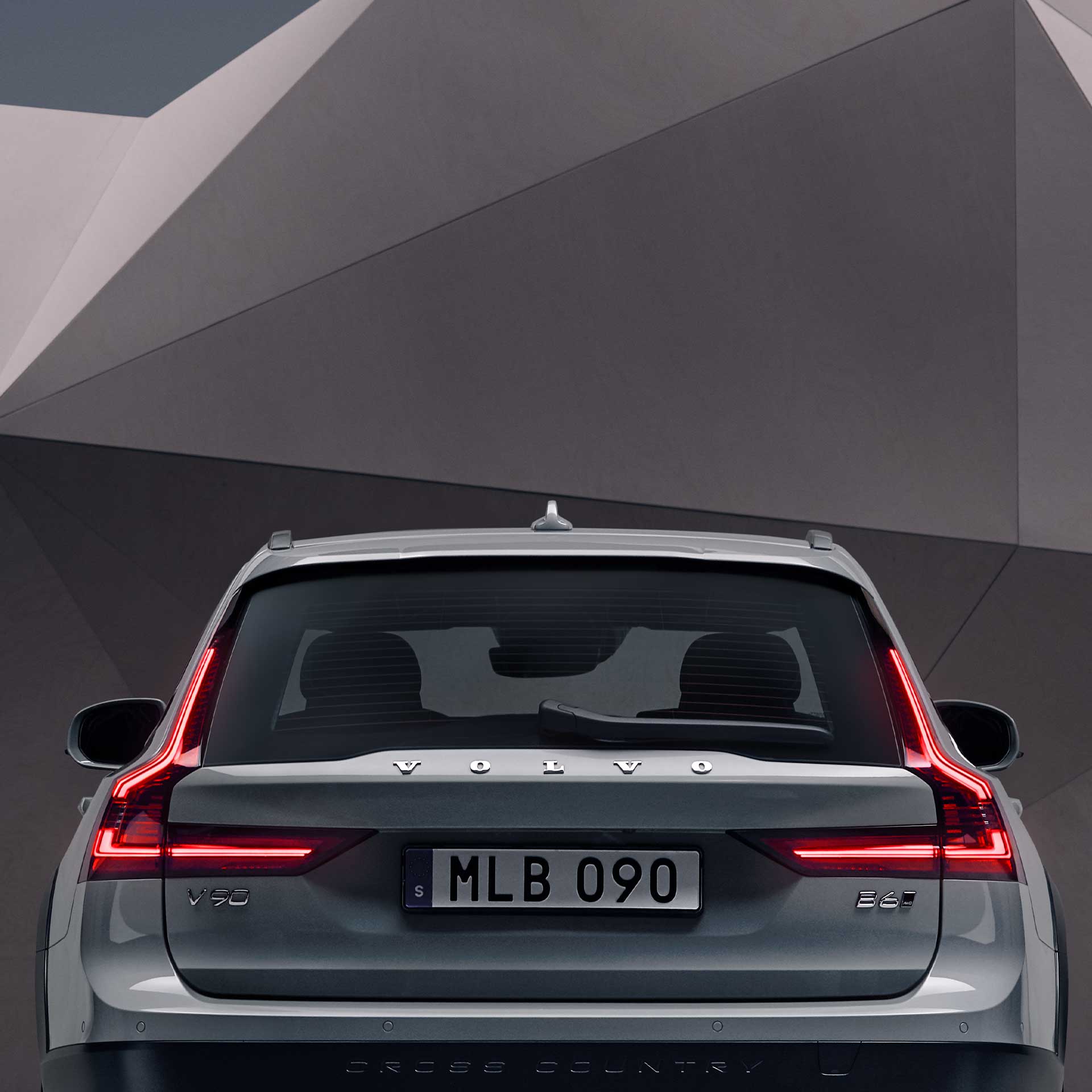 The rear exterior of a grey Volvo V90 Cross Country standing in front of an artistic wall.