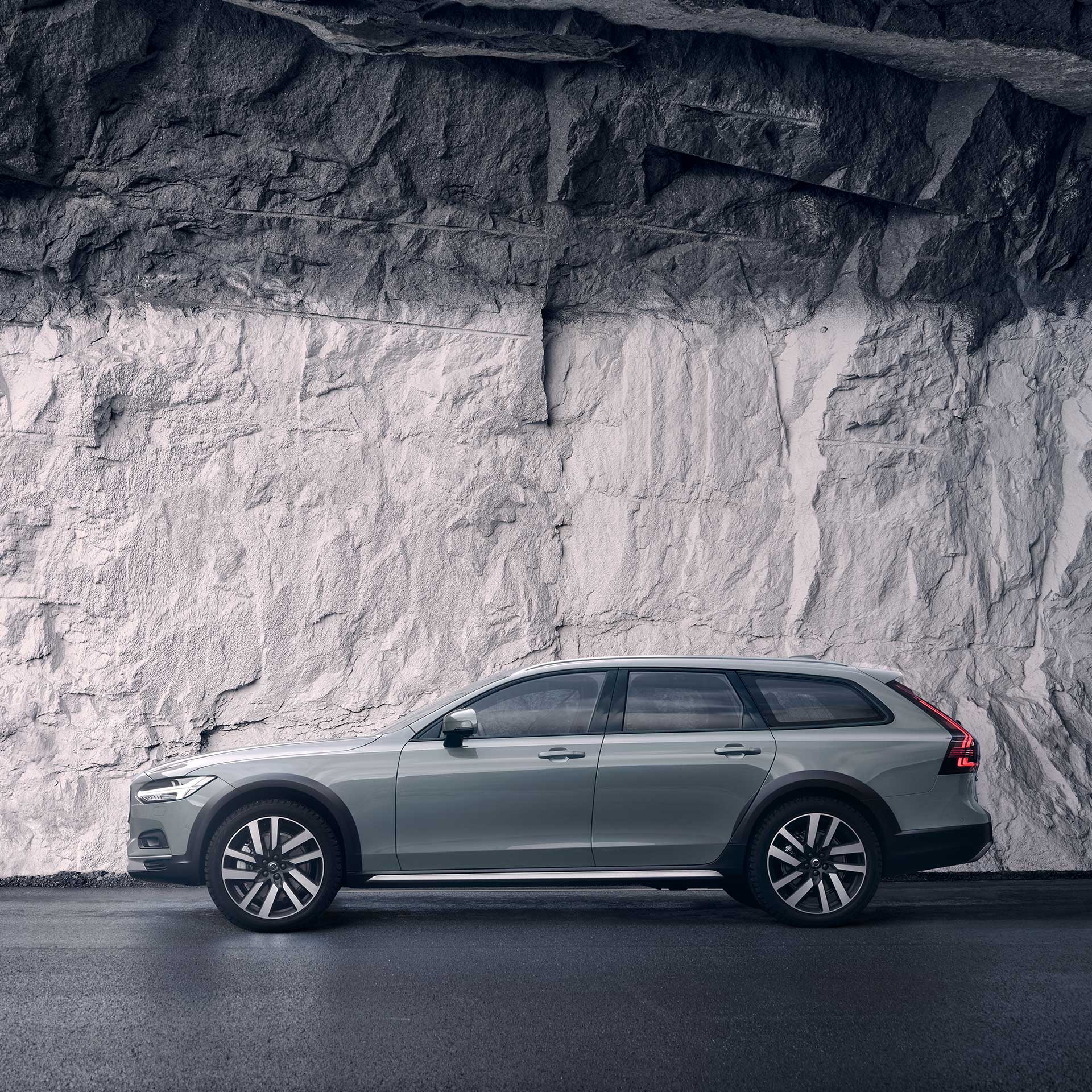 A grey Volvo V90 Cross Country parked against a rock wall.
