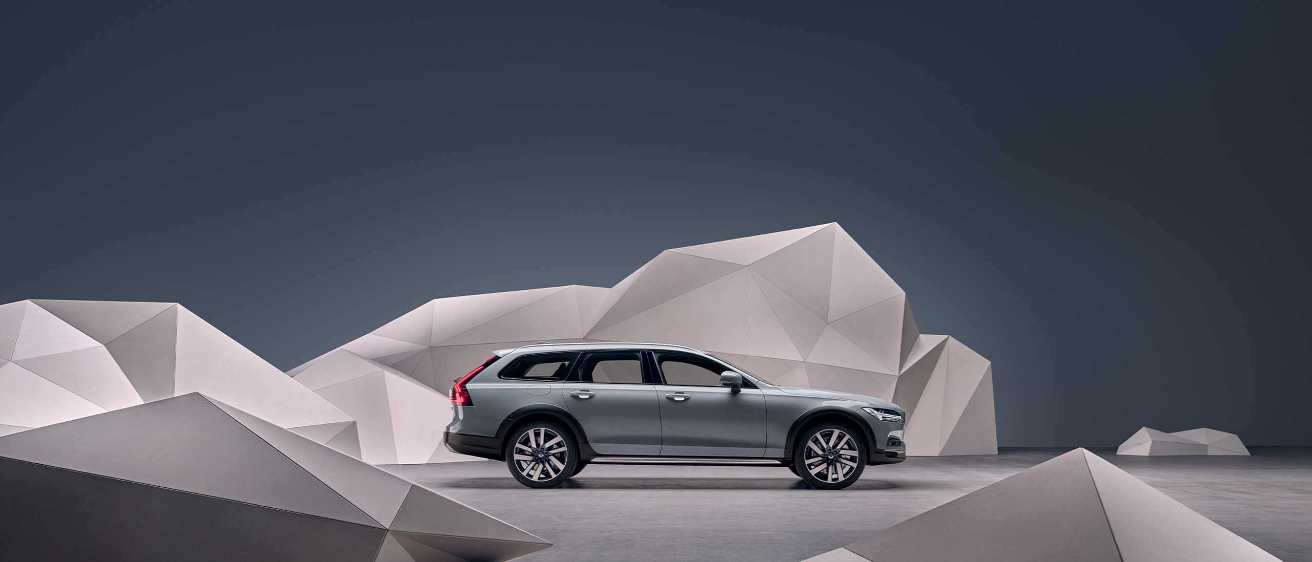 A grey Volvo V90 Cross Country standing in front of an artistic wall.