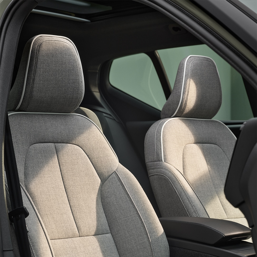 Sedadla předního spolujezdce a řidiče plug-in hybridního vozu Volvo XC40 Recharge opatřená šedým čalouněním Tailored Wool Blend s příměsí vlny a bílým lemováním.