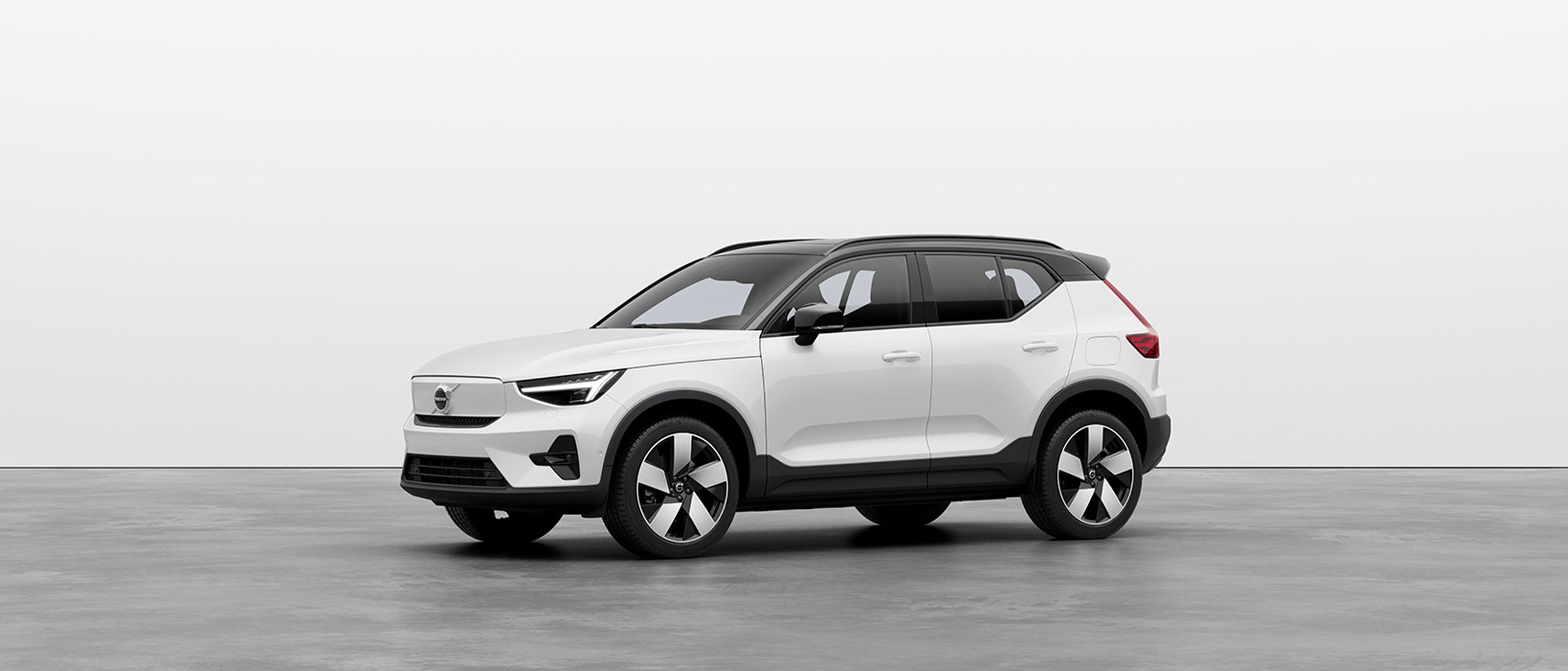 A white Volvo XC40 Recharge SUV standing still on grey floor in a studio.