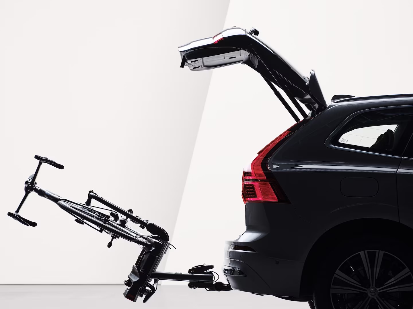 An open tailgate and a bicycle holder attached by tow bar folded down on the rear of a Volvo XC60.