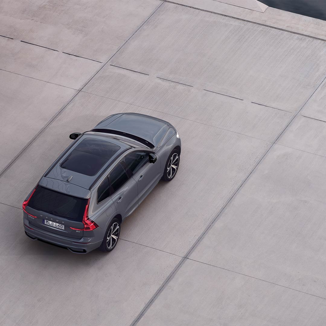 A silver Volvo XC60 with a panoramic roof next to a rock wall.
