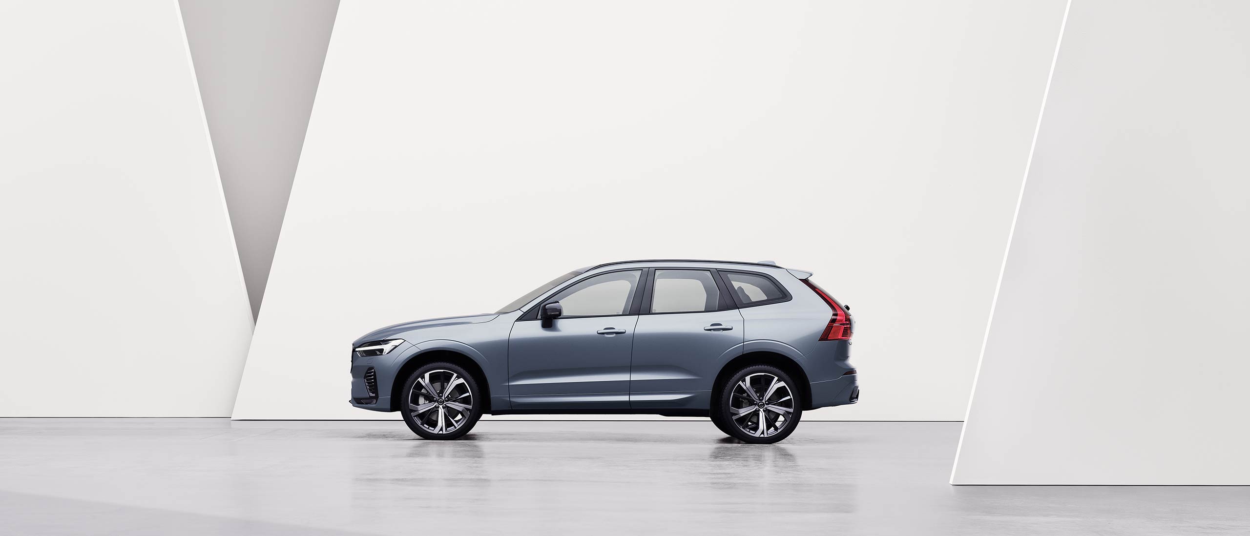 A silver Volvo XC60 standing still in front of a rock wall.