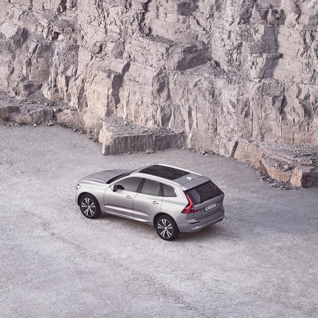 Srebrn Volvo XC60 s panoramsko streho poleg skalnate stene.