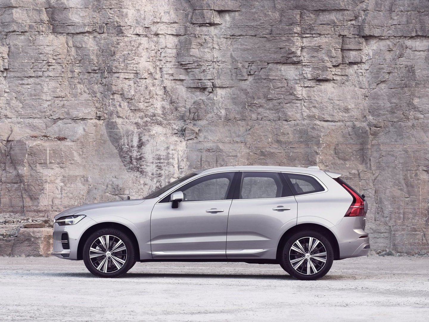 A silver Volvo XC60 standing still in front of a rock wall.