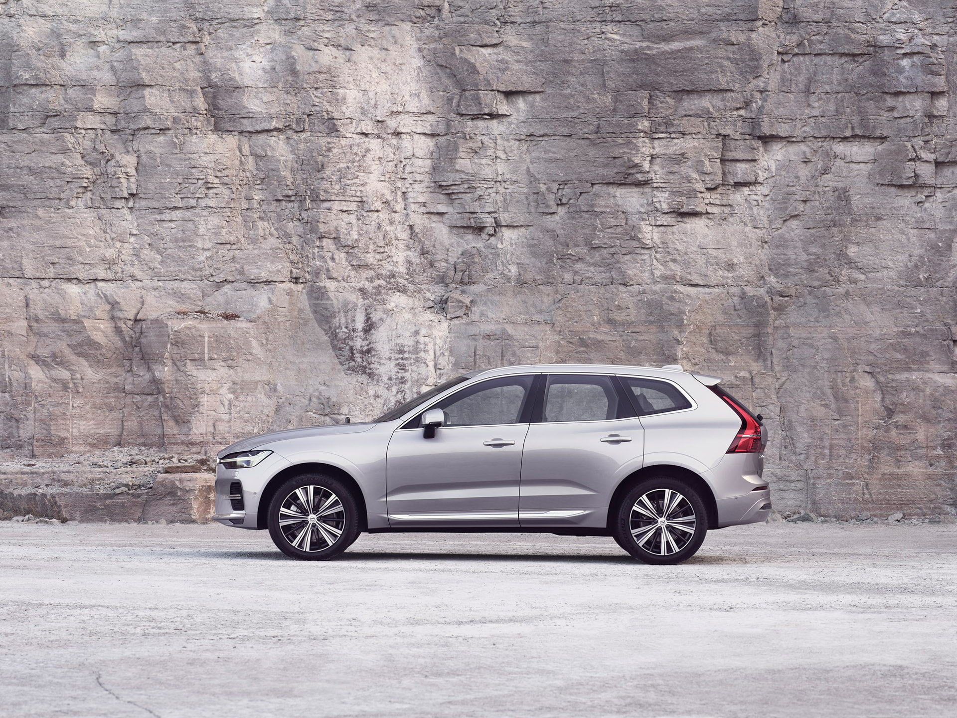 Серебристый Volvo XC60 стоит на фоне каменной стены.