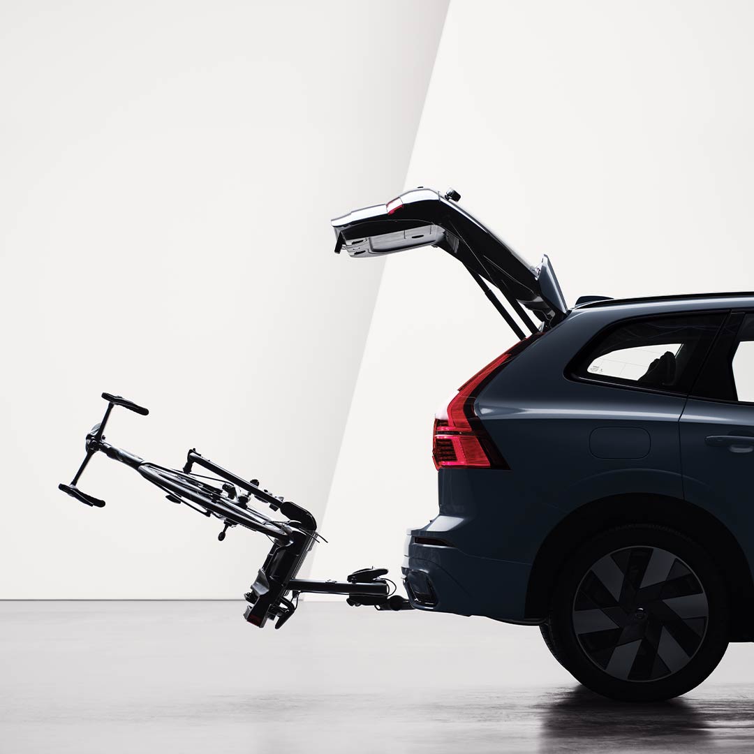 An open tailgate and a bicycle holder attached by tow bar folded down on the rear of a Volvo XC60 Recharge. 